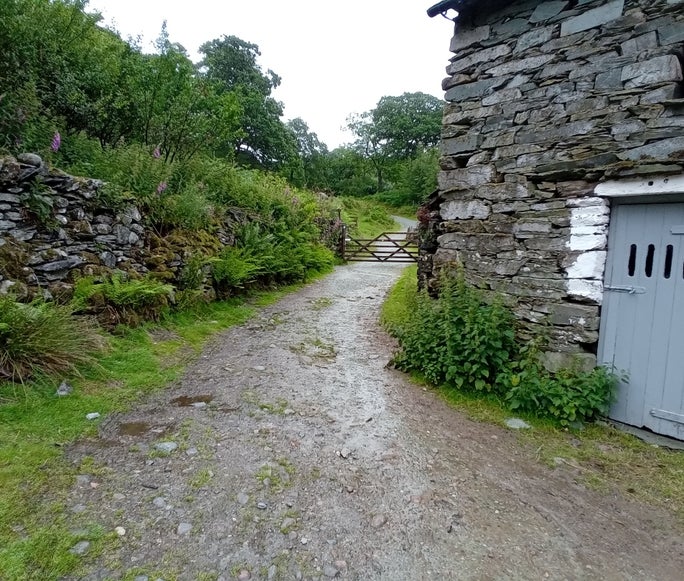 A wooden gate across a stony footpath next to a farm building, Tilberthwaite, Cumbria