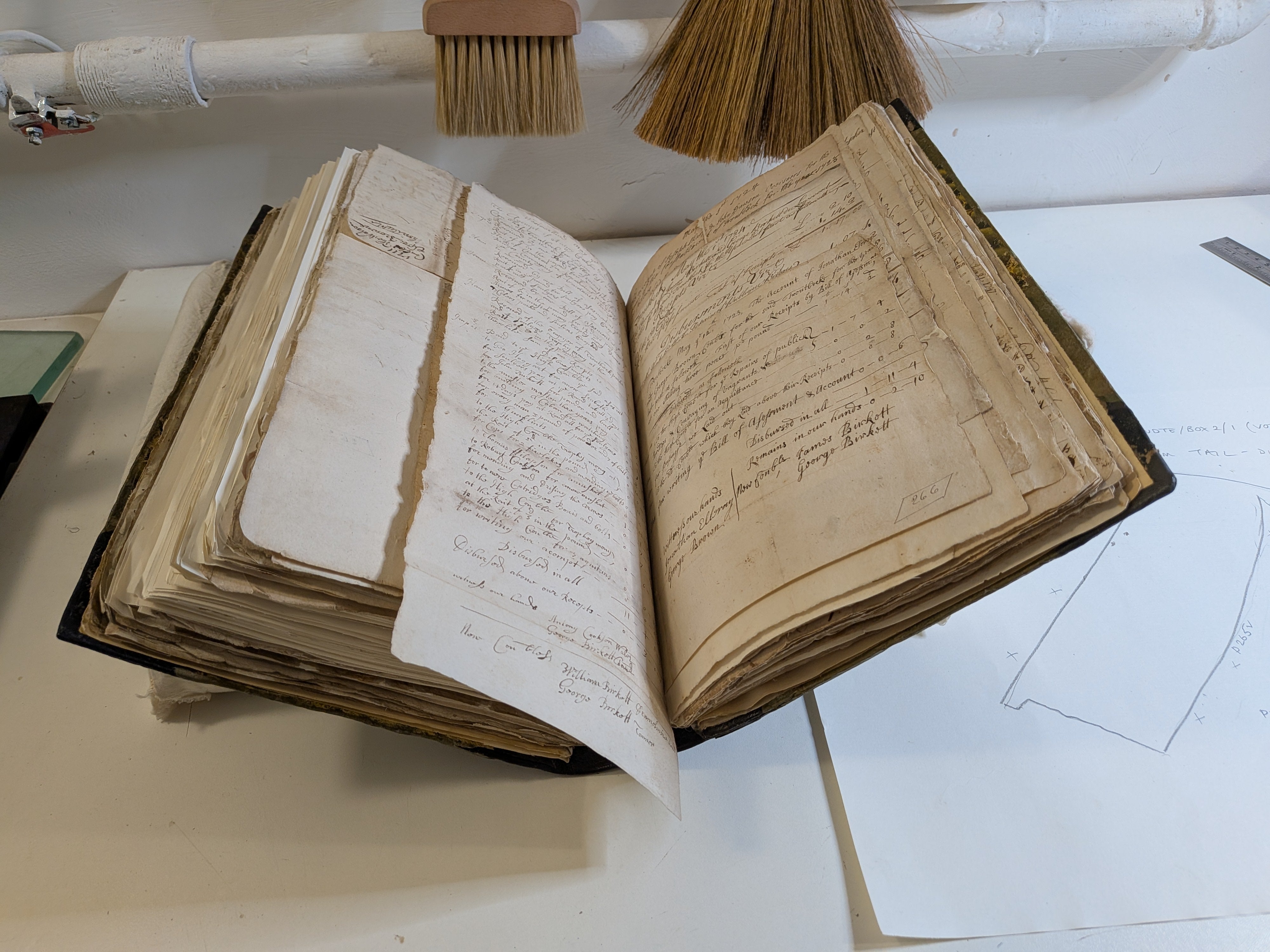 An old handbound book with documents in lies open on a stand on a table.