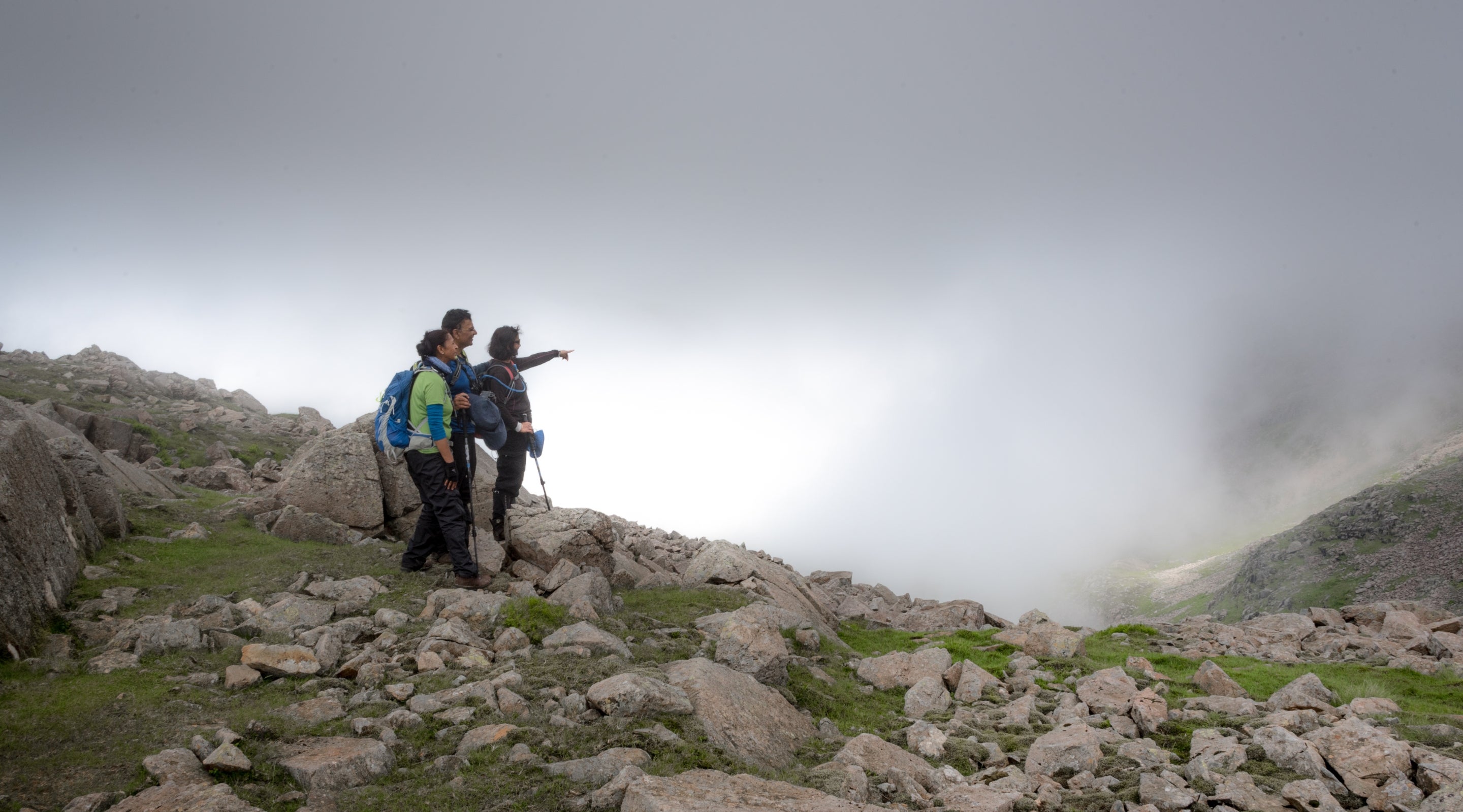 Hikers point out towards Great End from near the summit of Scafell pike on a misty summer's day