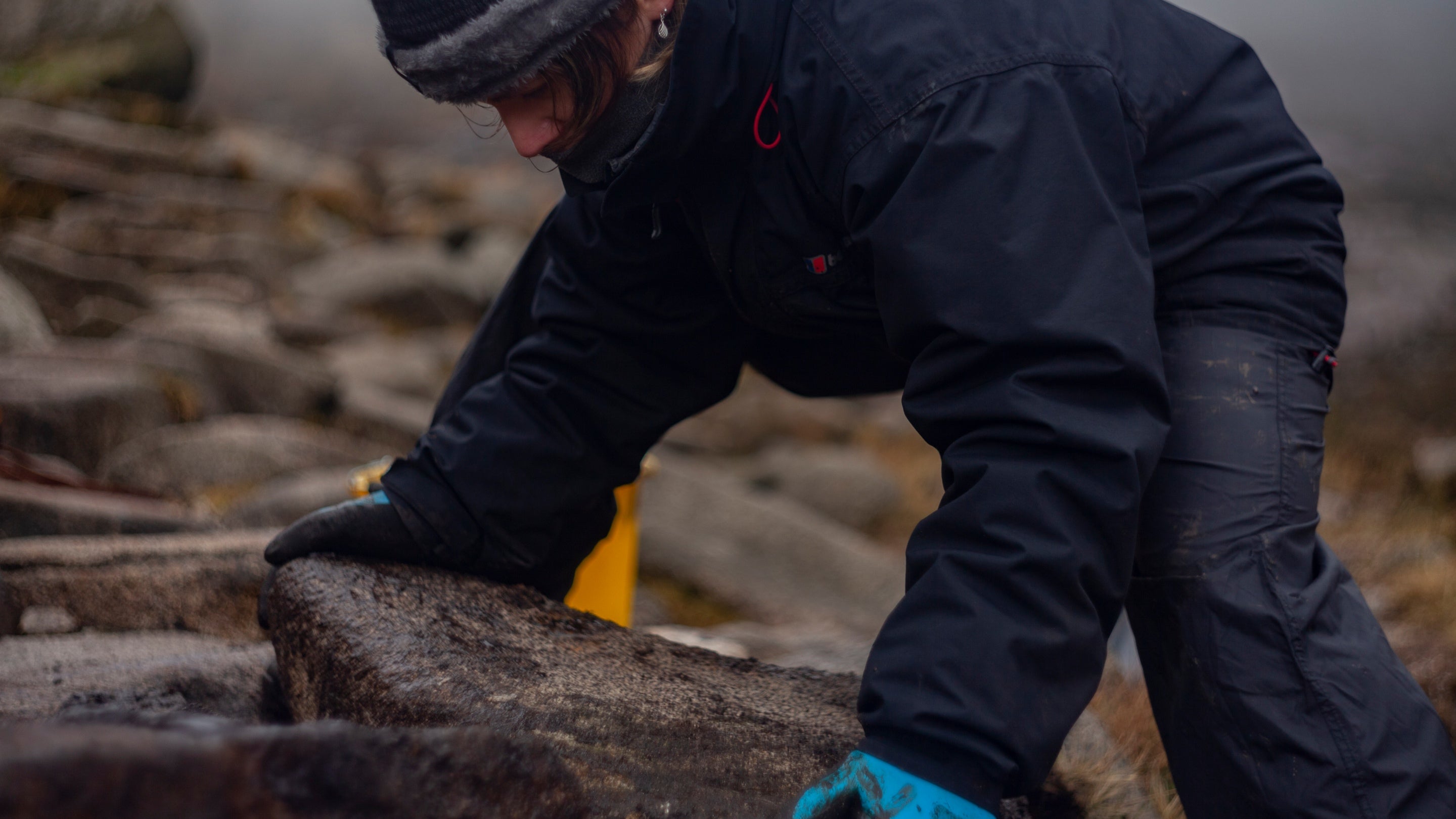 A National Trust ranger positions a large stone on a mountain footpath during restoration work