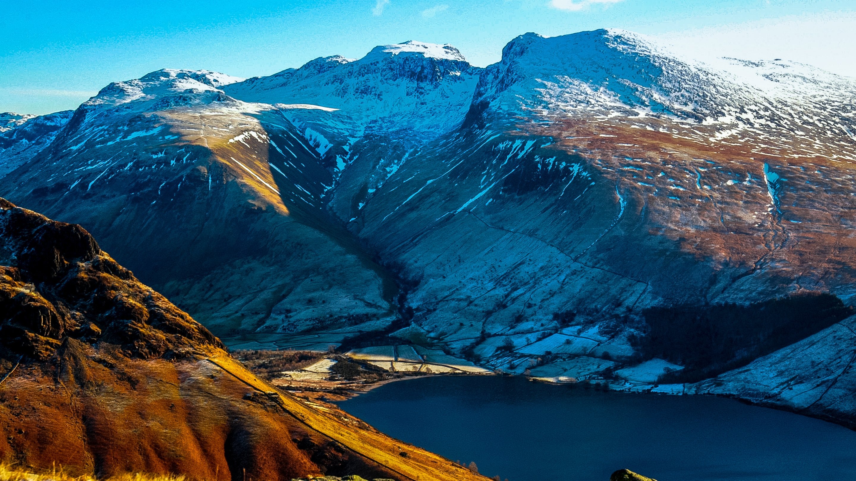 Winter view of Scafell Pike from Wasdale, Cumbria. Snow capped mountains sit against a clear blue sky.