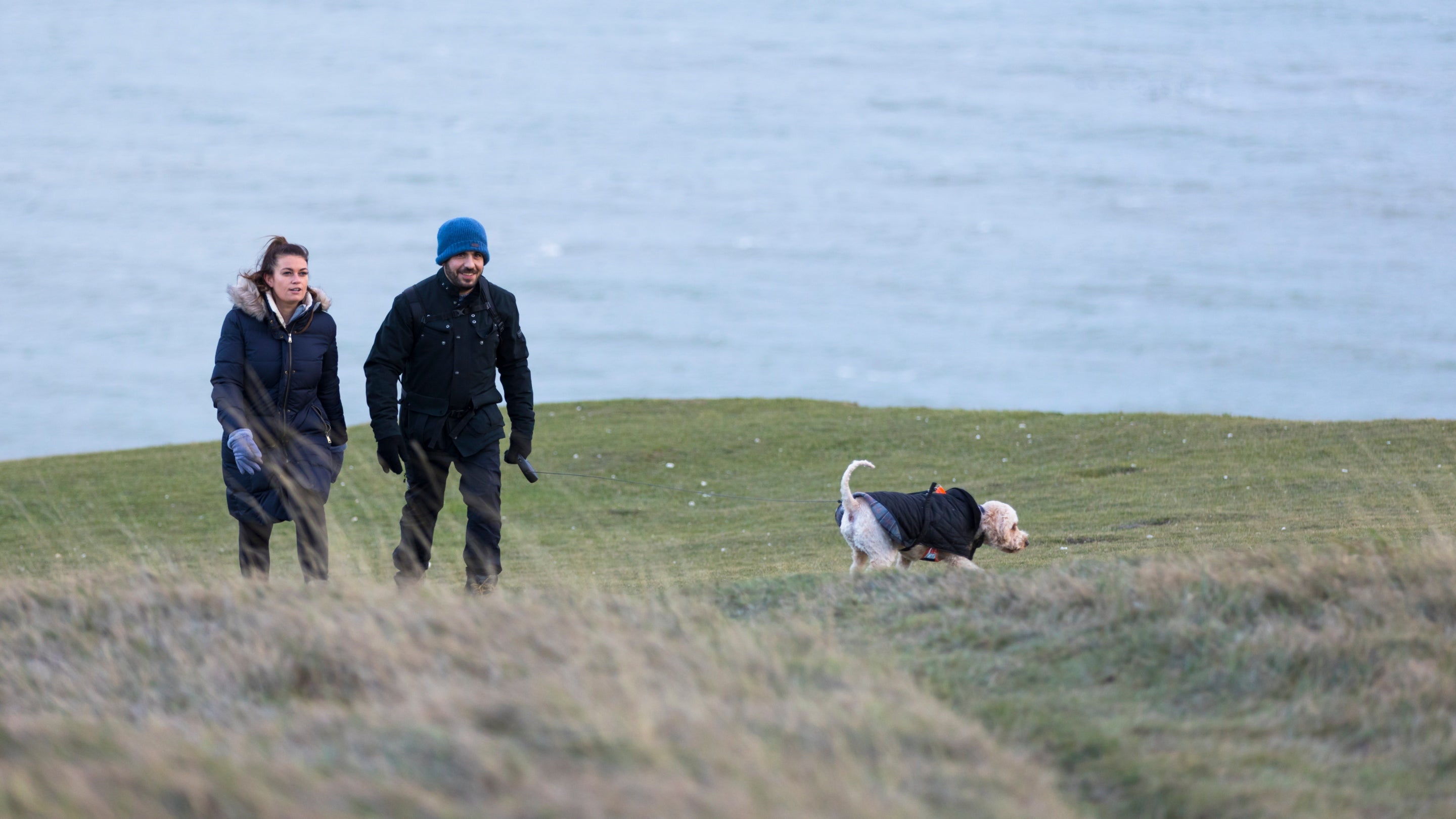 Two visitors explore the coastal path on the Whitehaven Coast with their dog during winter