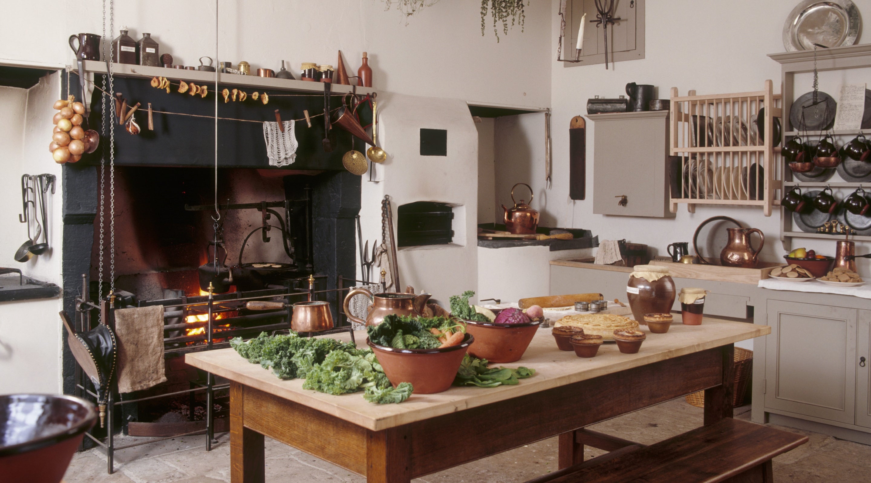View of the kitchen and fire place where herbs have been brought in to dry and autumn vegetables are being prepared on the table