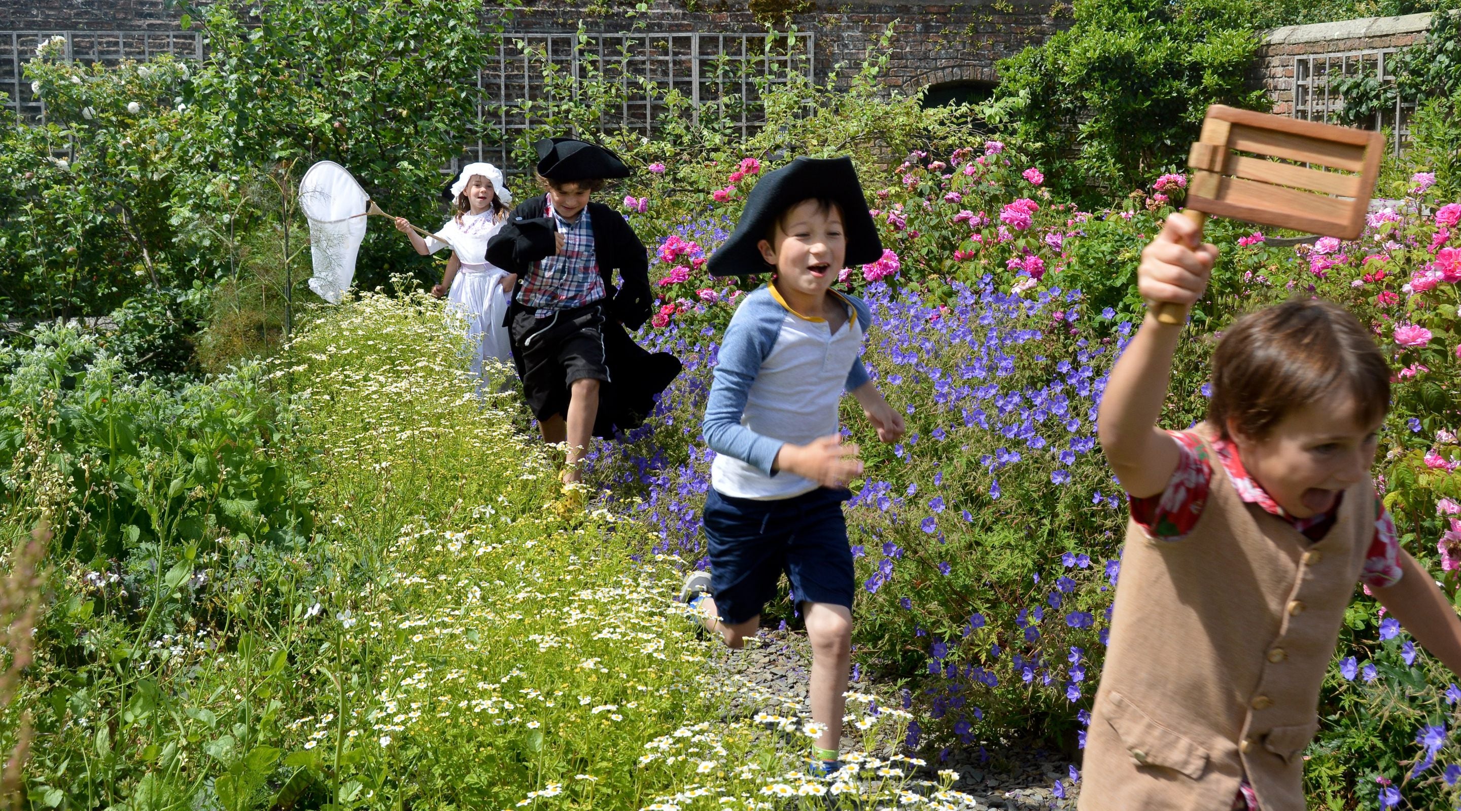 Children running through the garden on a sunny day dressed up in Georgian clothing