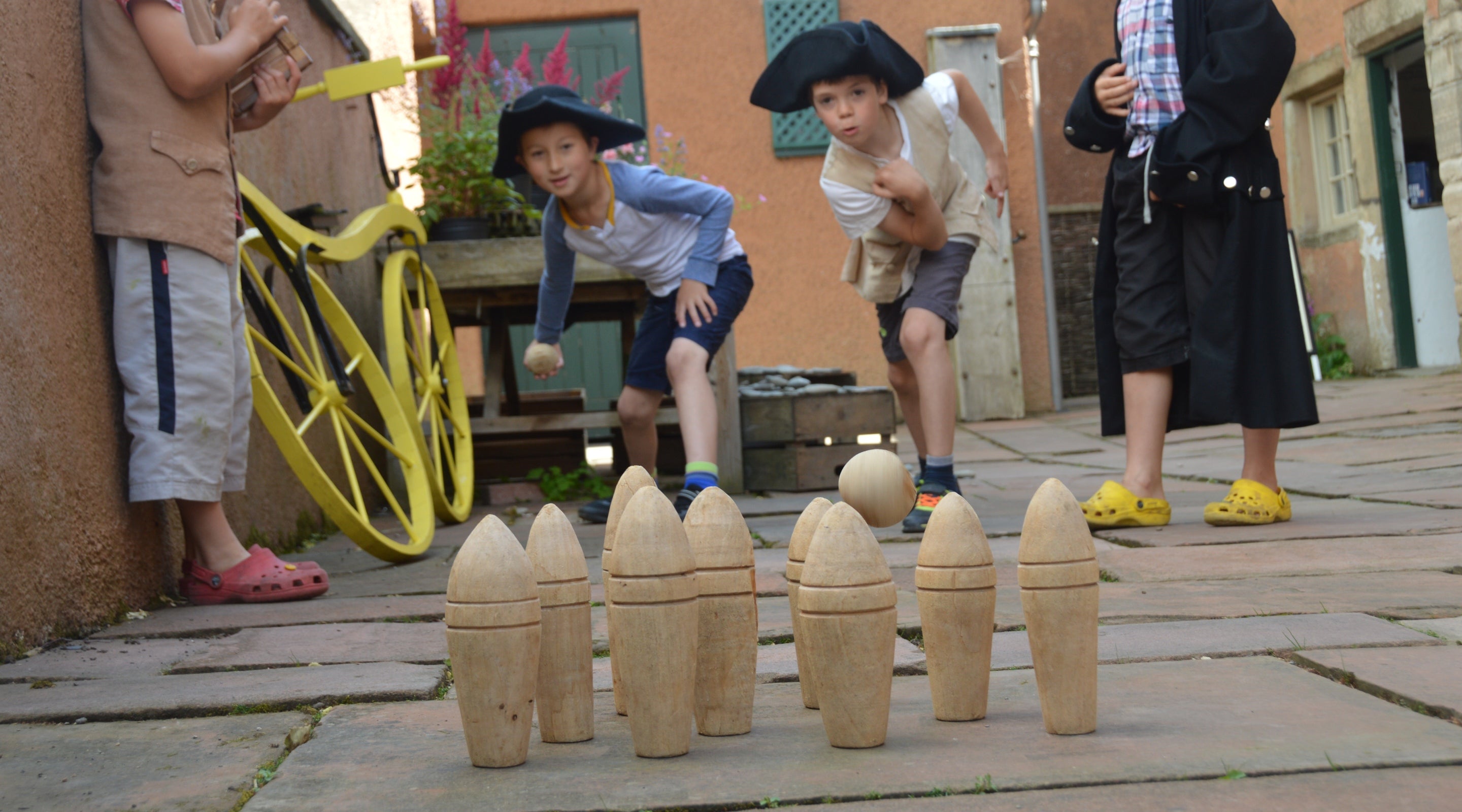 Children dressed in Georgian dress up clothes playing with a wooden bowling set in the garden at Wordsworth House and Garden