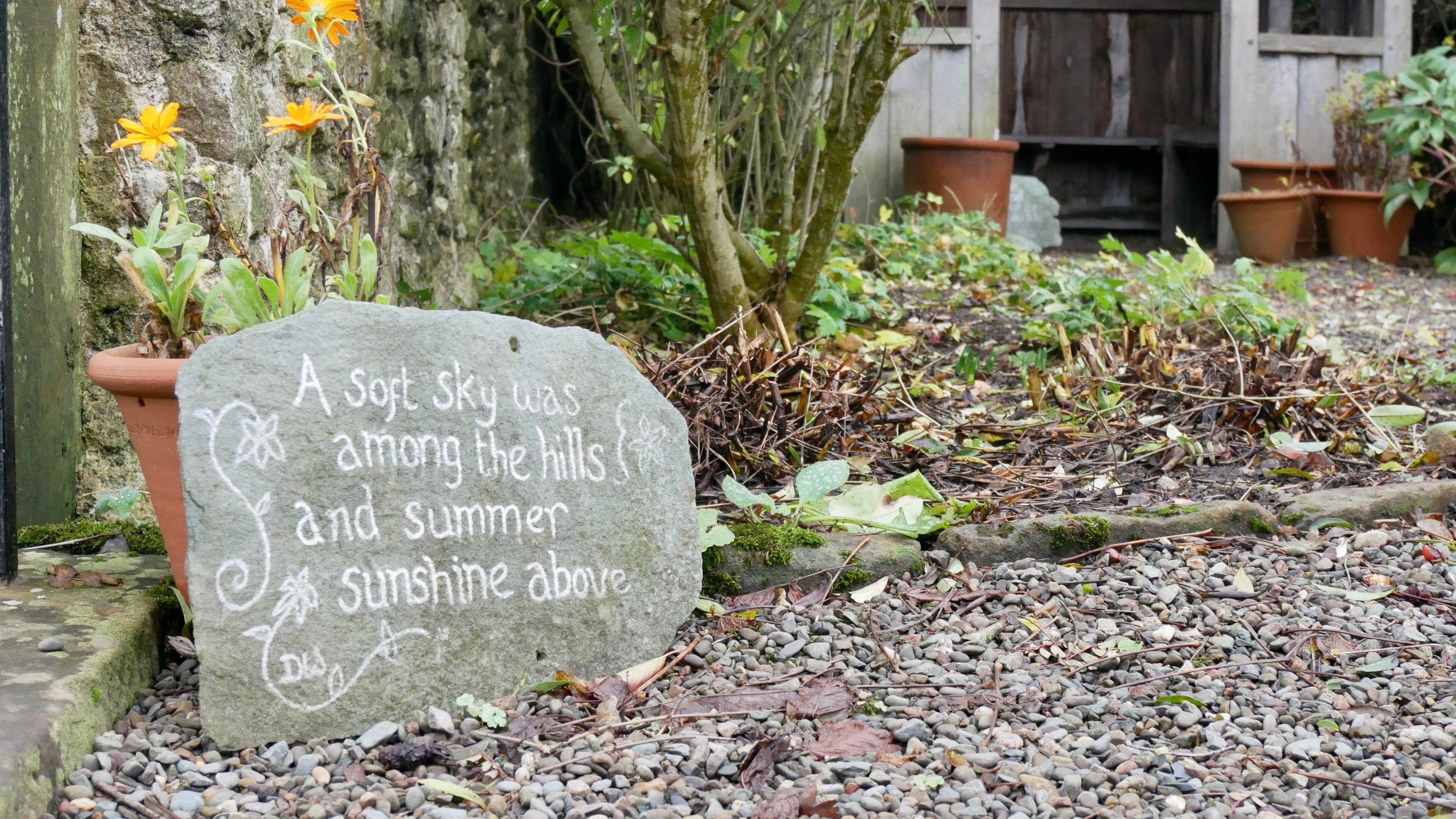 A potted marigold and a decorative garden slate on the raised terrace in the garden at Wordsworth House, Cockermouth. The verse on the slate reads 'a soft sky was among the hills and summer sunshine above'.