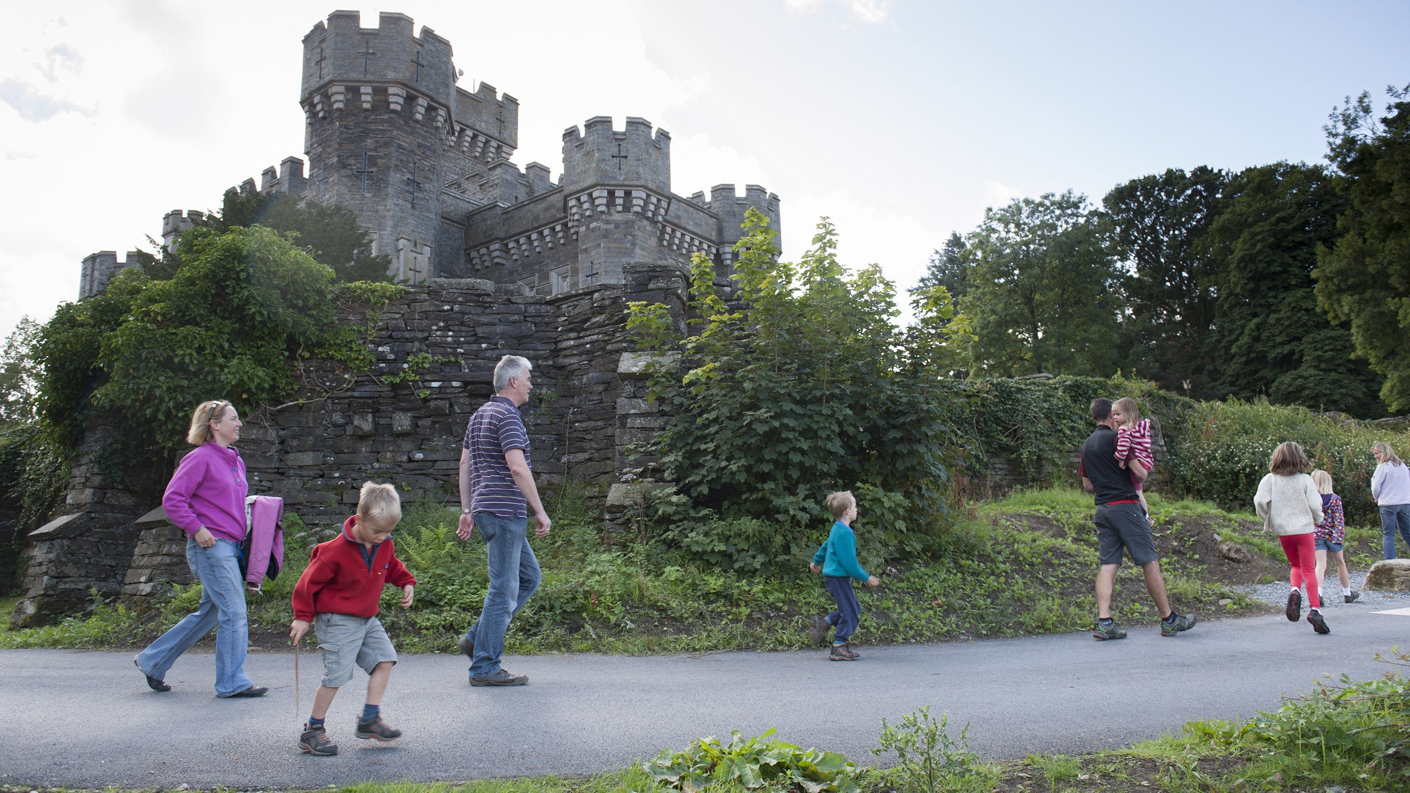A family pass under Wray Castle on a path during a walk in Cumbria