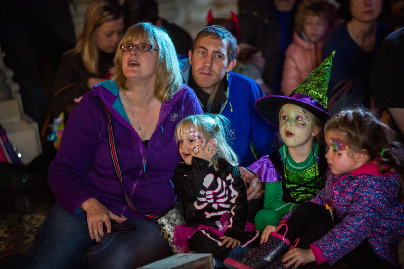 An audience including an enthralled family of five, the children are in Hallowe'en costumes and have painted faces.