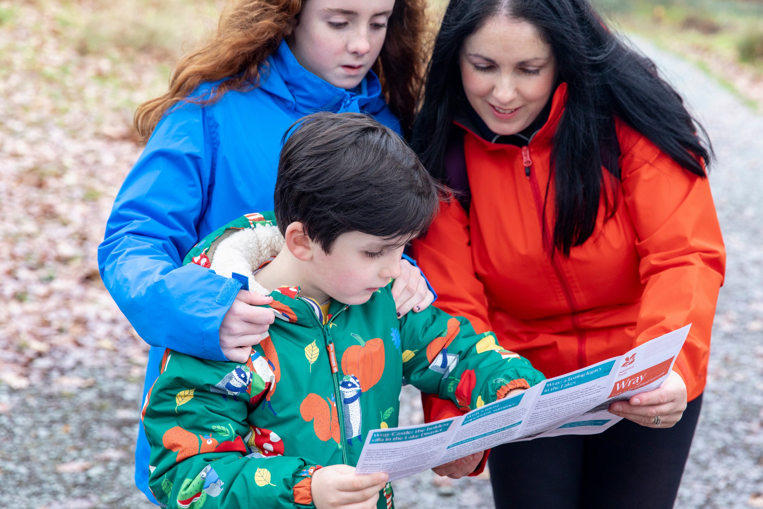 A family of three, dressed for an autumnal walk, gather around a trail sheet