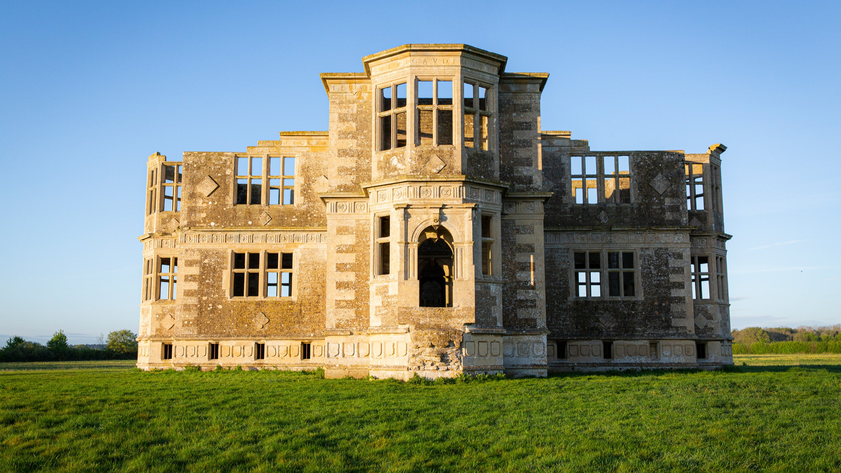 Lyveden's garden lodge surrounded by green grass stands tall in the spring sun.