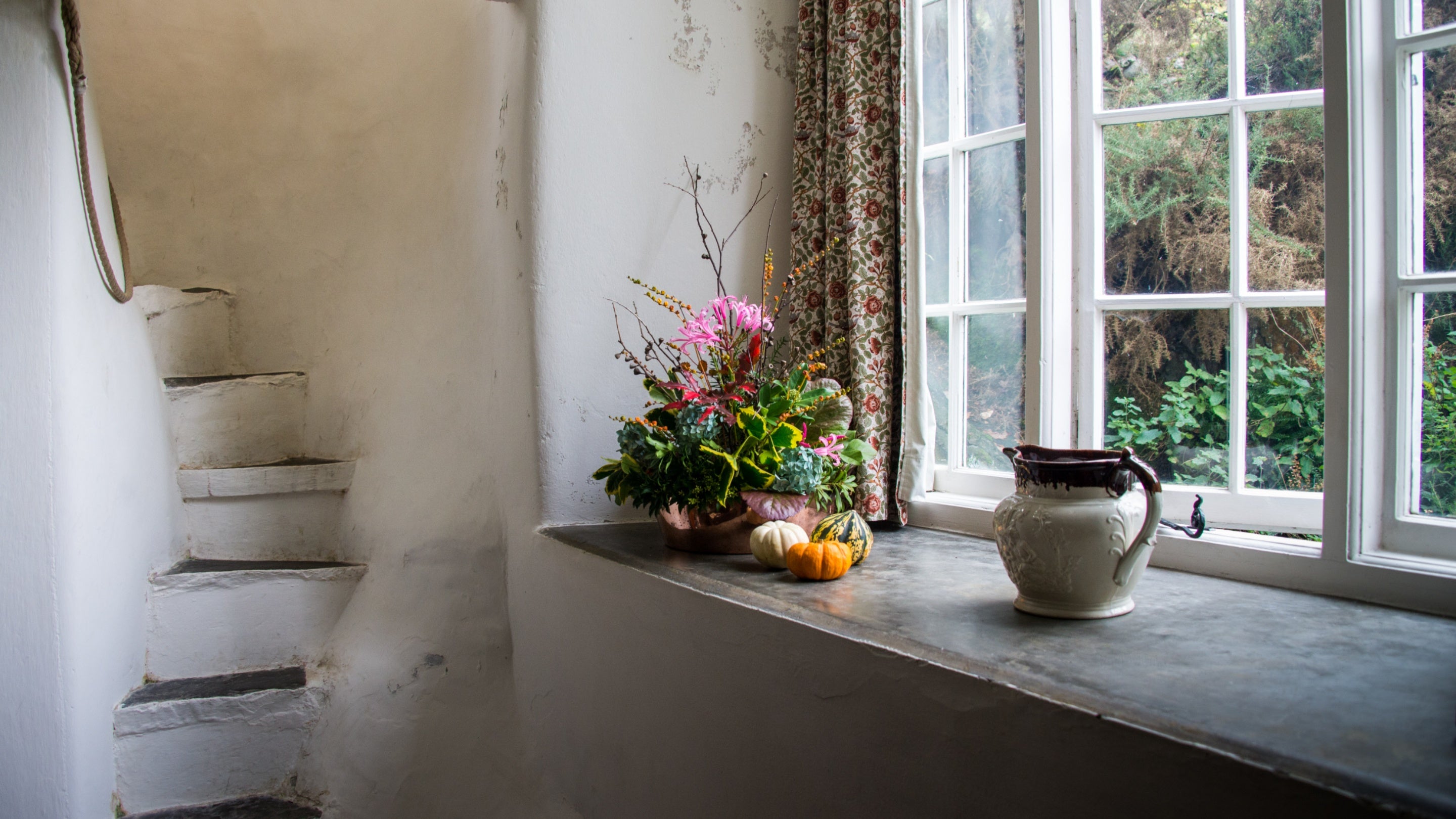 A display of autumnal gourds and flowers on a windowsill inside the cottage at Stoneywell, with a tiny staircase built into the cottage wall to the left.
