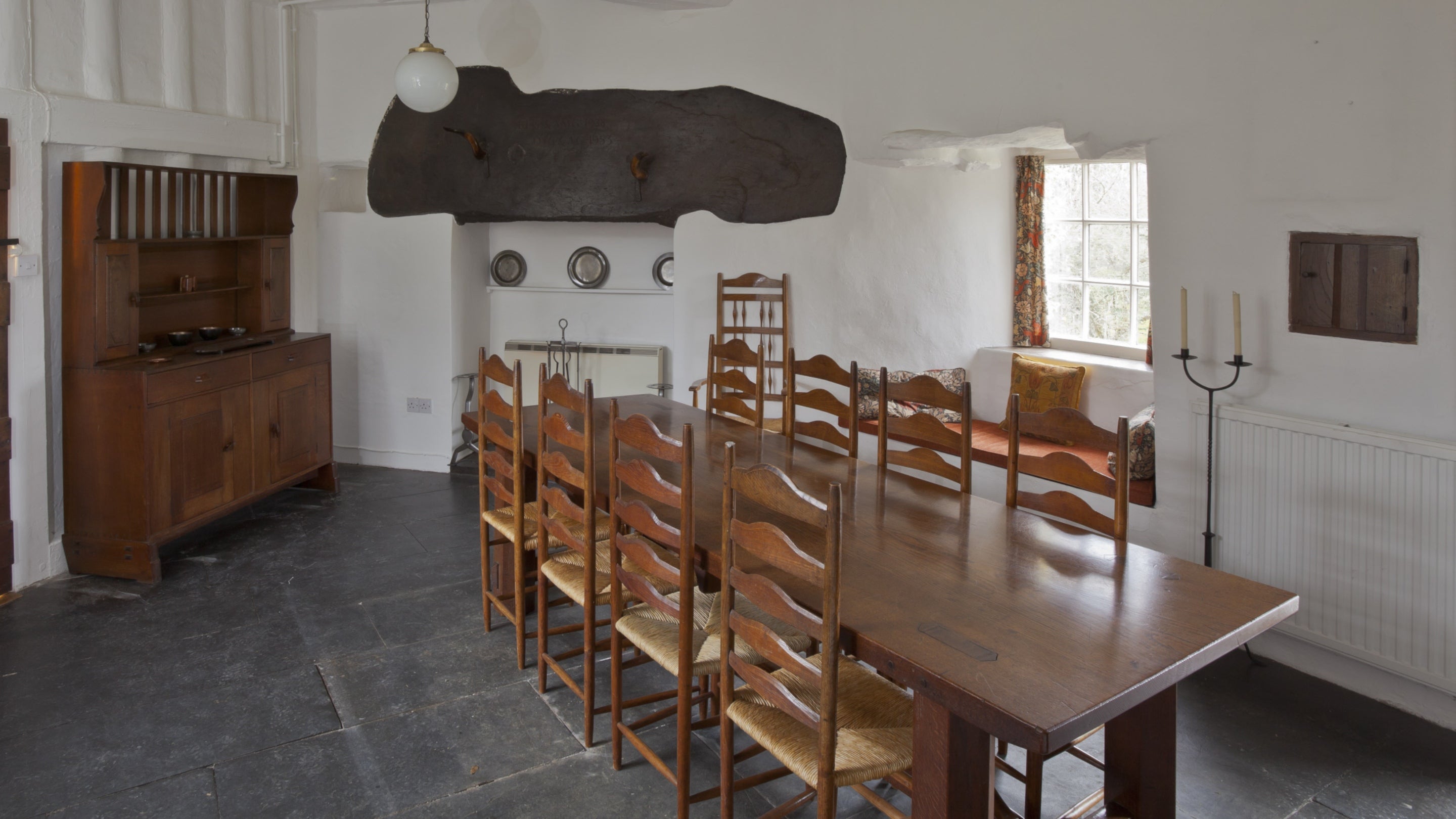 The Dining Room at Stoneywell with a large wooden table in the centre, surrounded by eight Ernest Gimson chairs and a wooden cabinet in the background