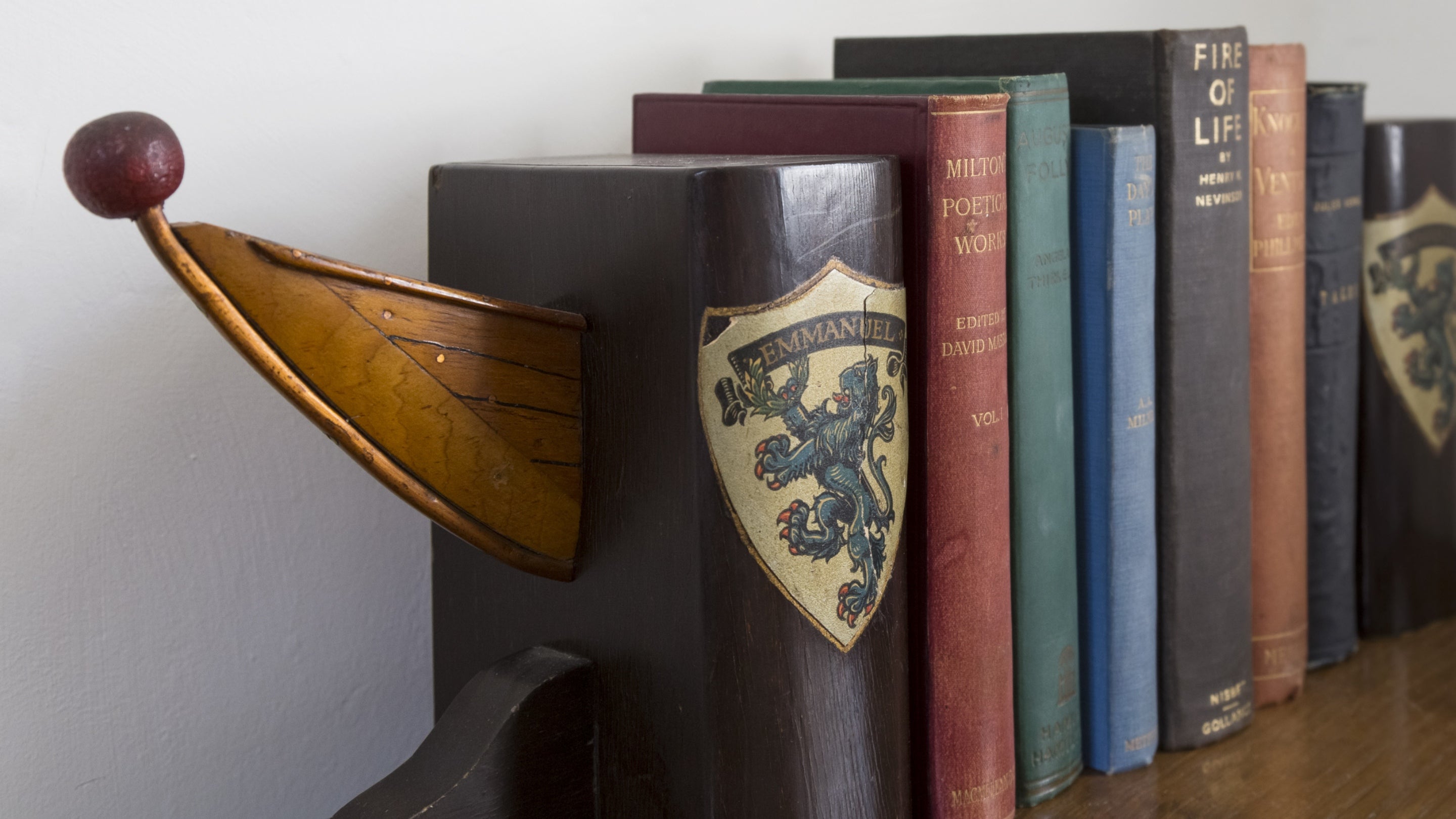 A pair of wooden bookends bearing the crest of Emmanuel College, Cambridge, in a bedroom at Stoneywell, with books propped between them