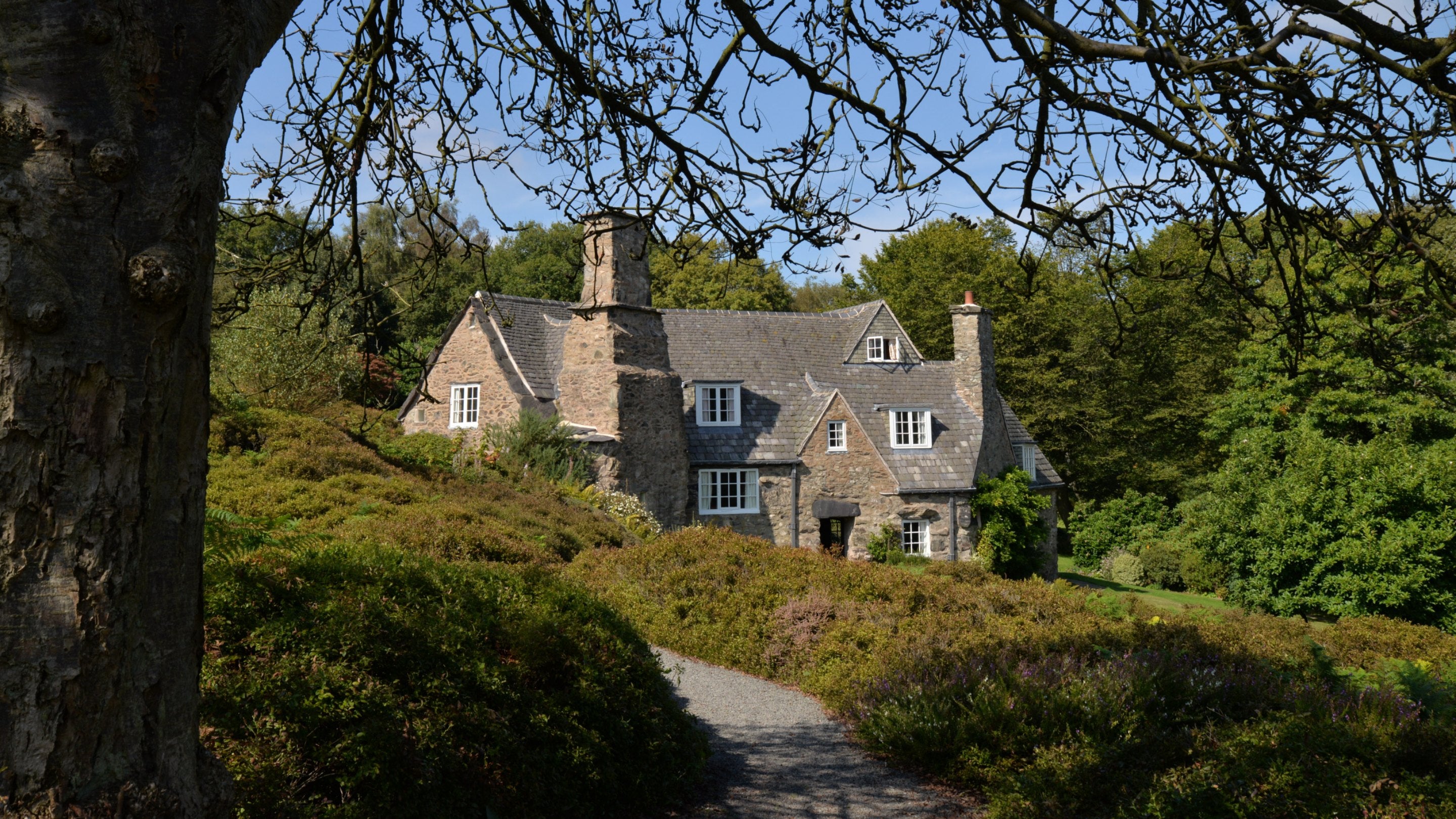 A view of Stoneywell from the garden, with a footpath in the foreground and the cottage framed by trees and hedges