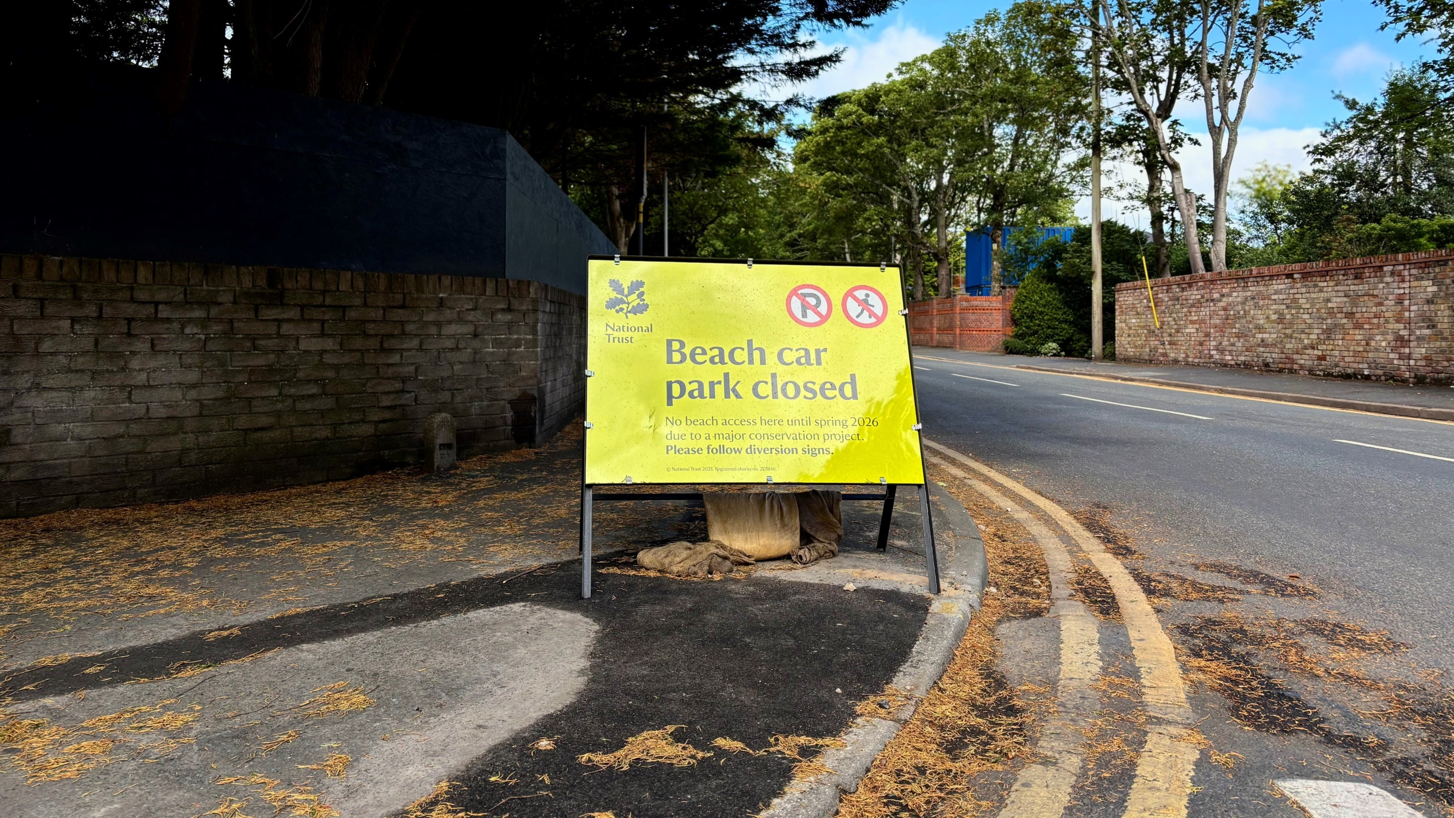 Bright yellow sign with the text Formby beach car park closed for a major conservation project until spring 2026. Also shows no parking or pedestrian access symbols