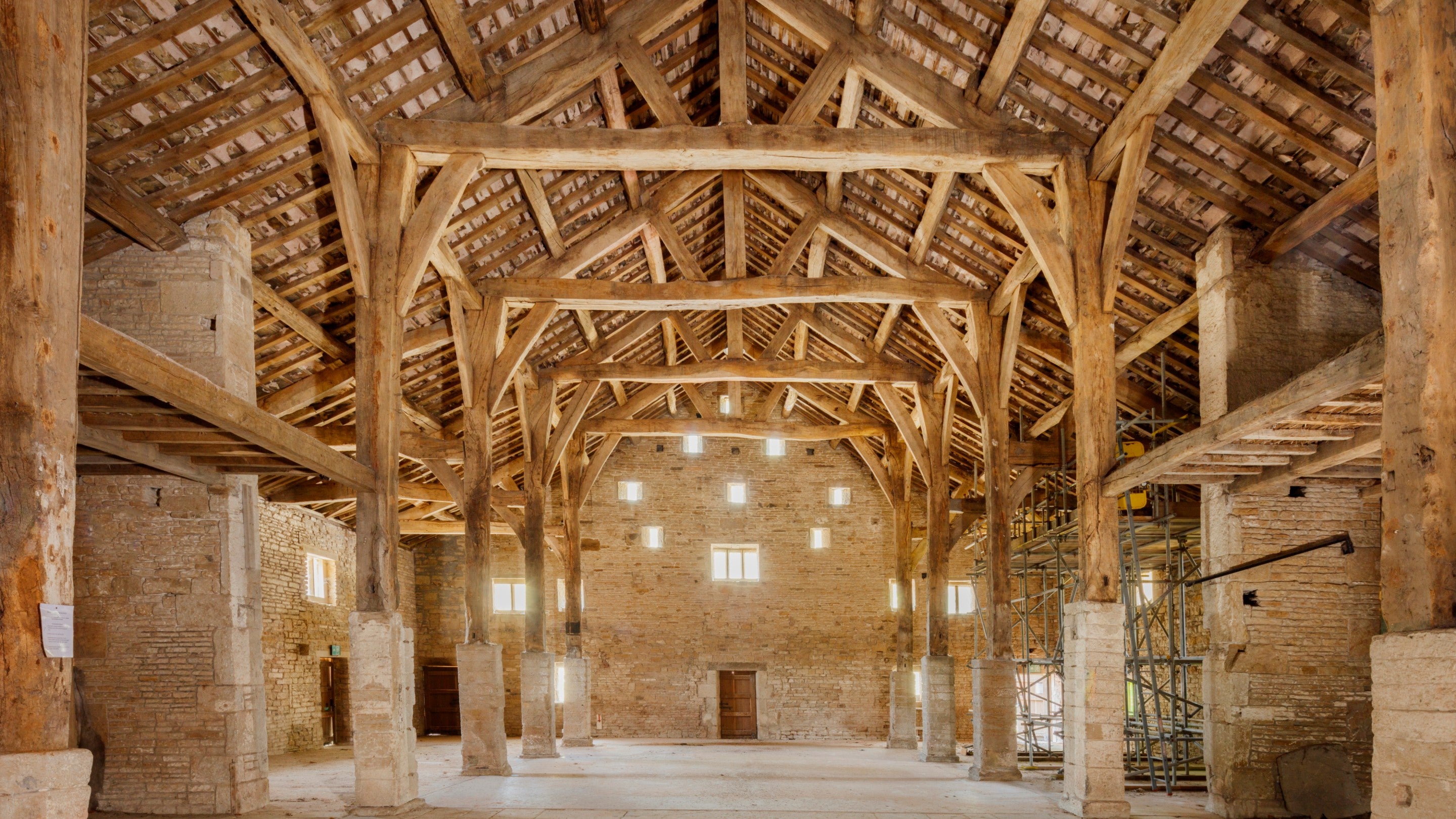 Interior of a large historic barn with exposed timber beams, stone walls, and high vaulted roof.