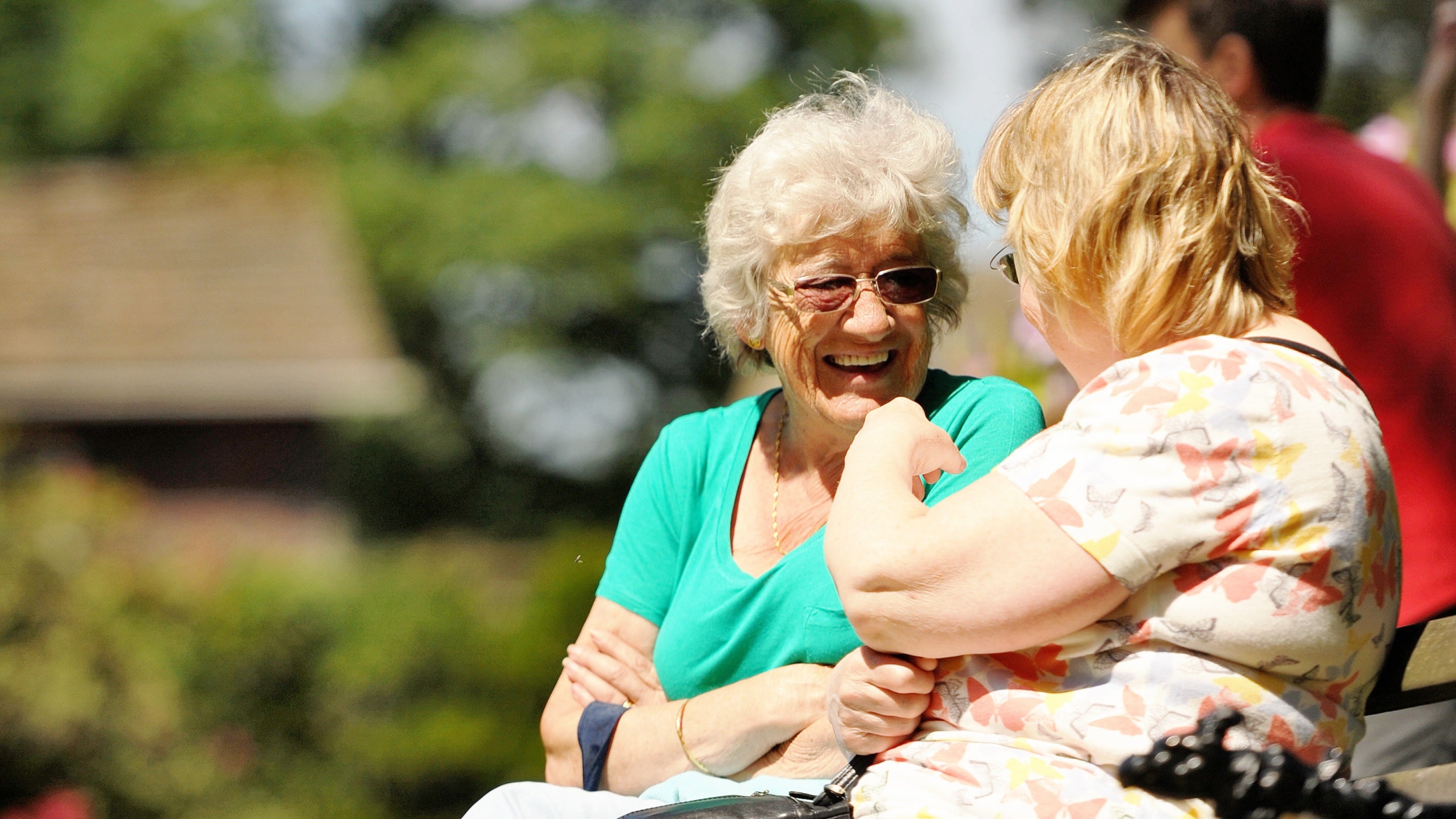 Close-up of two visitors smiling on a bench in the sunny garden at Rufford Old Hall in Lancashire.