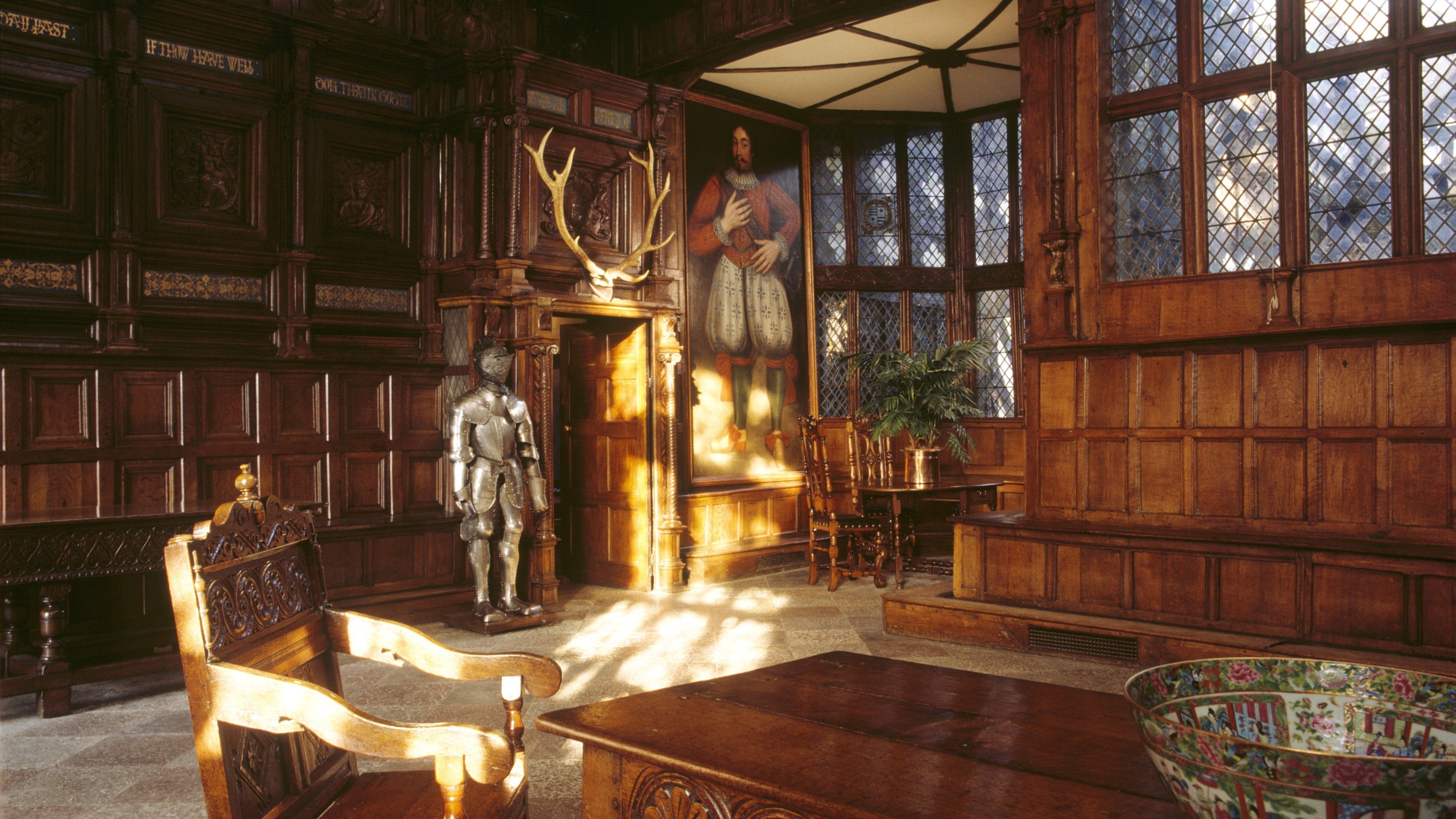 A view of the interior of the Great Hall at Speke Hall with a large portrait and a suit of armour