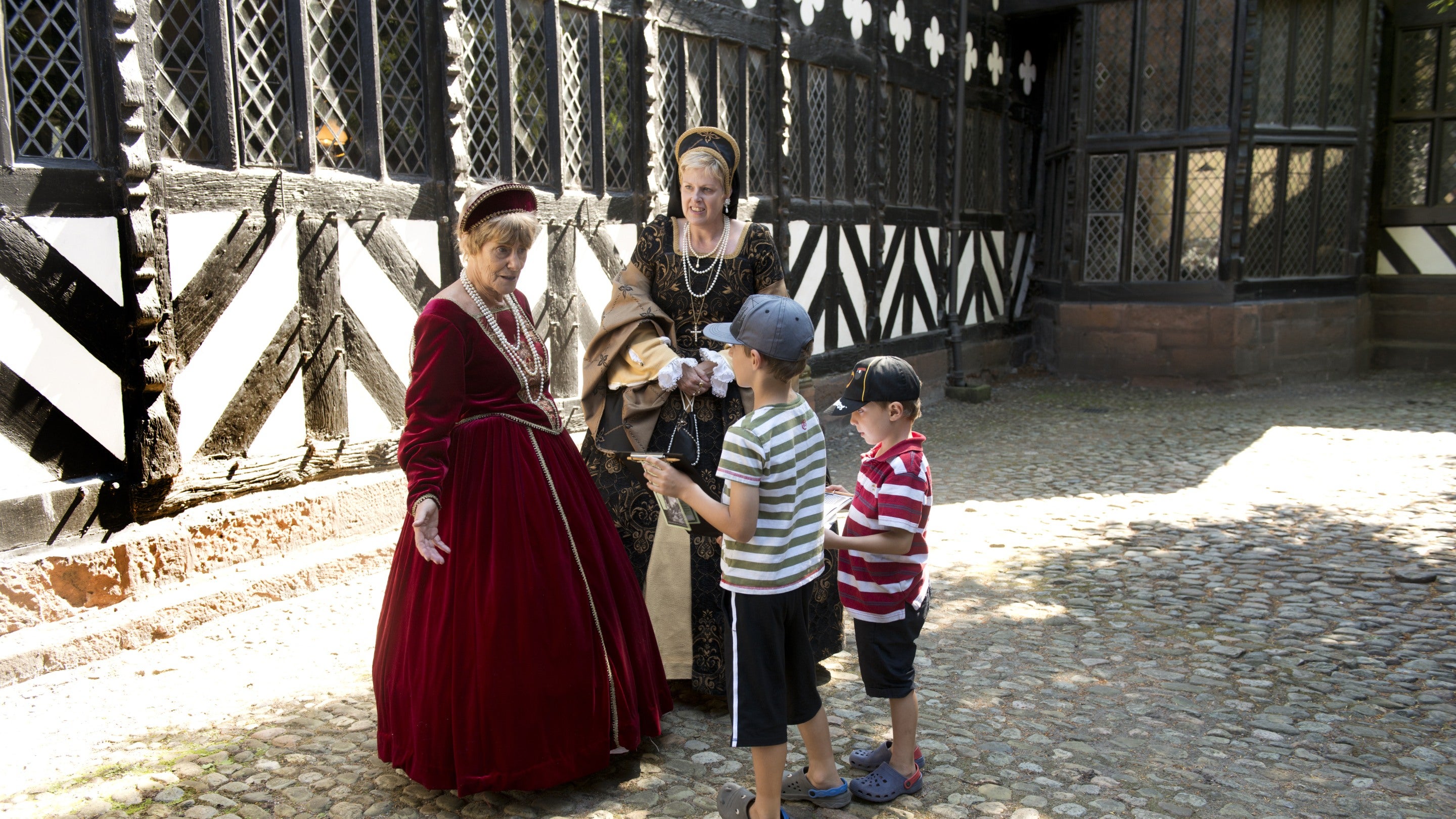 Two children talking to two costumed intepreters at Speke Hall with beamed building in the background
