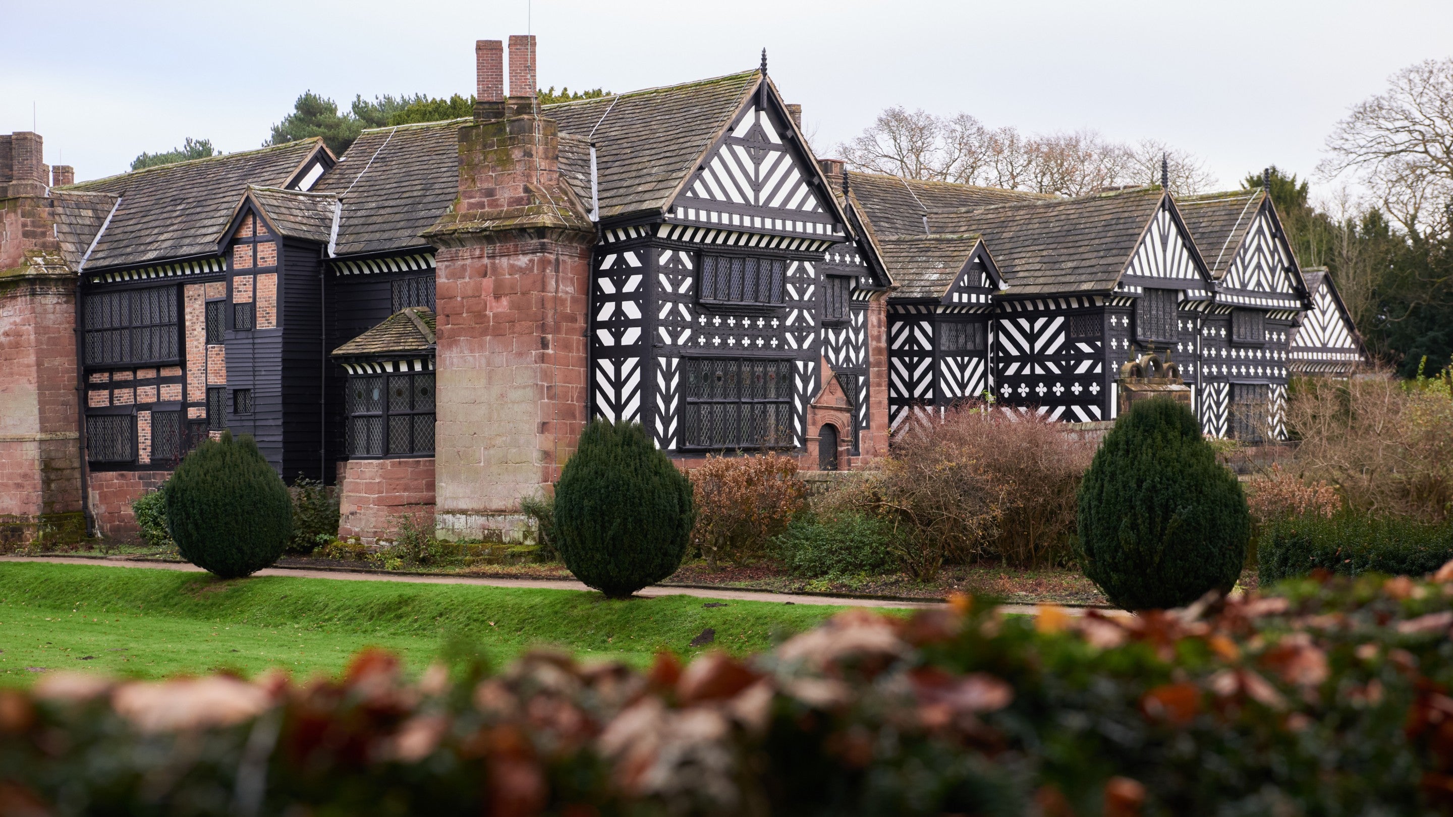 An exterior shot of a black and white Tudor house sat amongst well manicured greenery and shrubs.