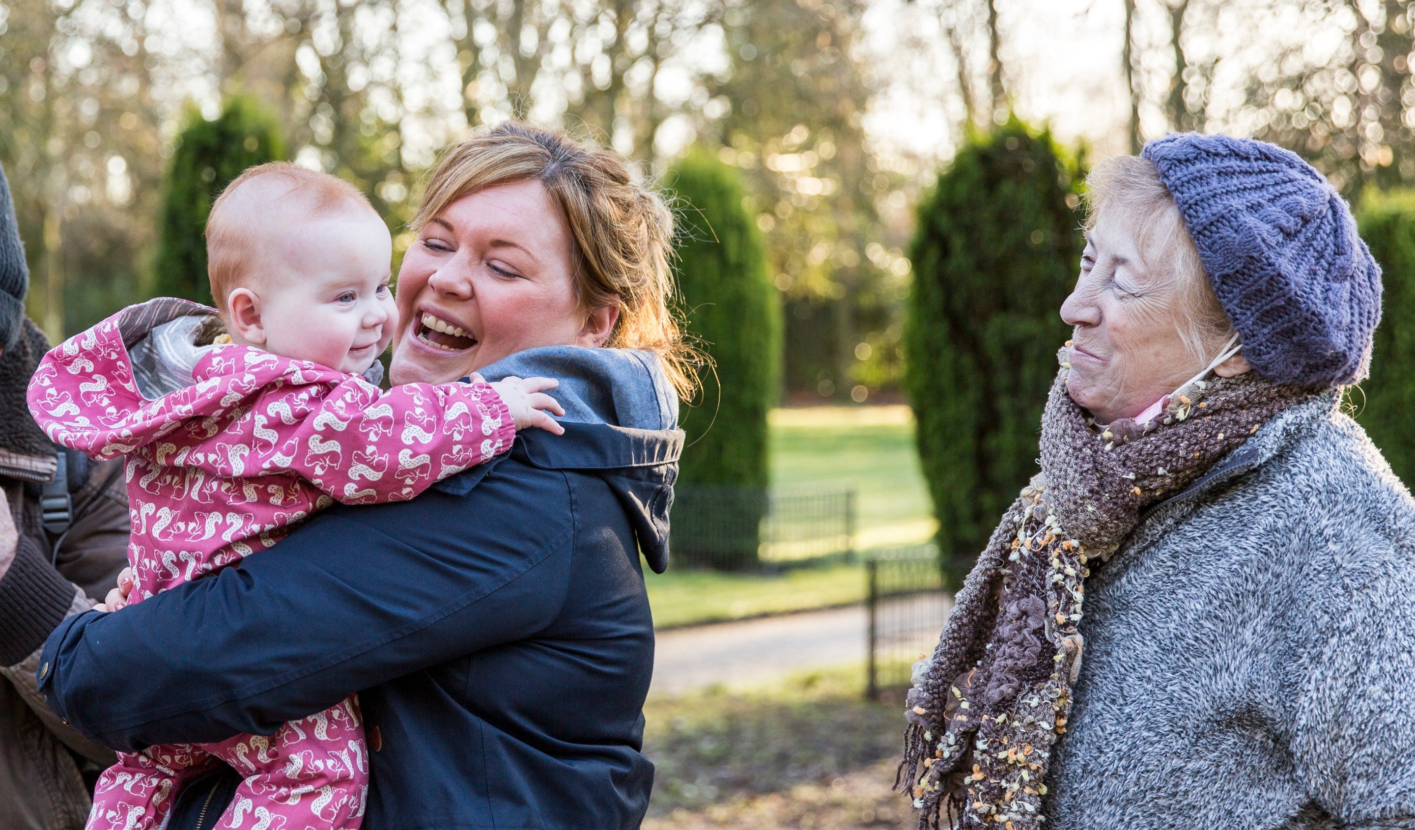 A multi-generational family in the garden at Speke. They are dressed for winter. A woman is smiling at a baby in her arms.