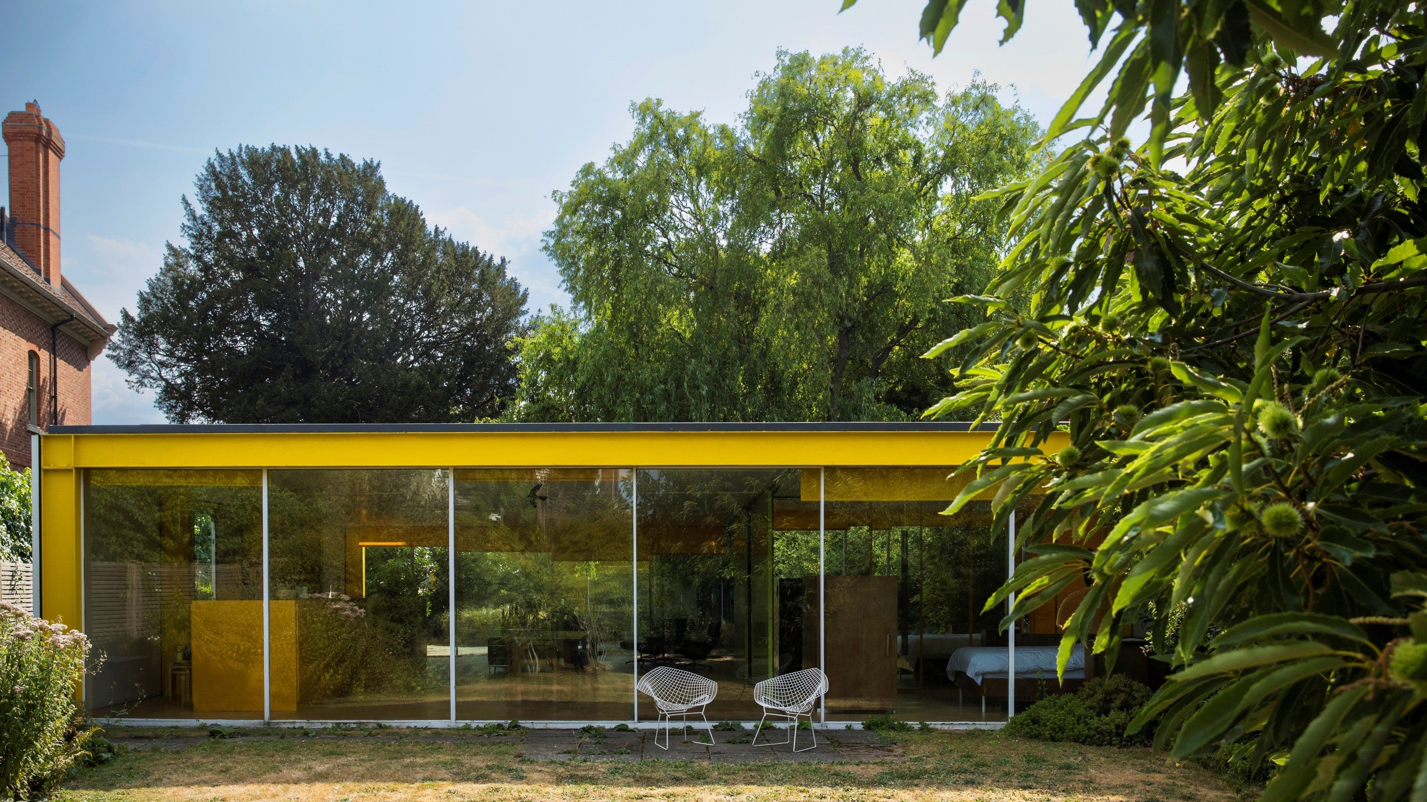 A single storey building with full floor to ceiling windows. The building has a vibrant yellow fascia. A large tree sit in the foreground to the right of the buisling. facia