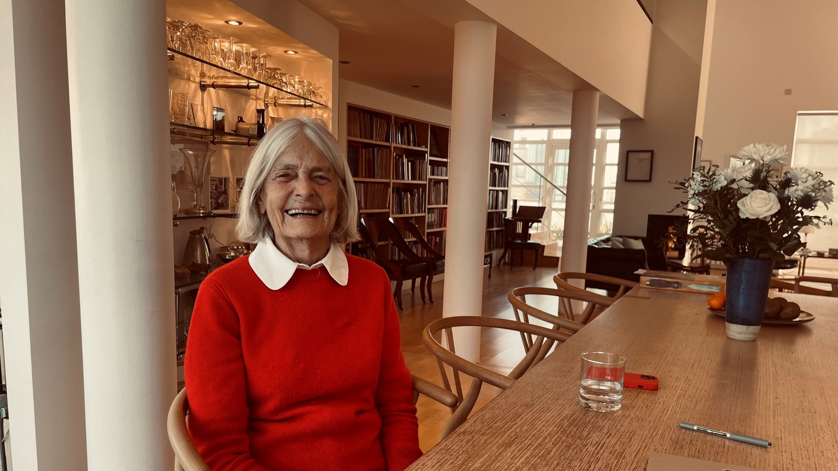 Su Rogers educator and co-designer is wearing a red jumper. She is sat at a dining room table.