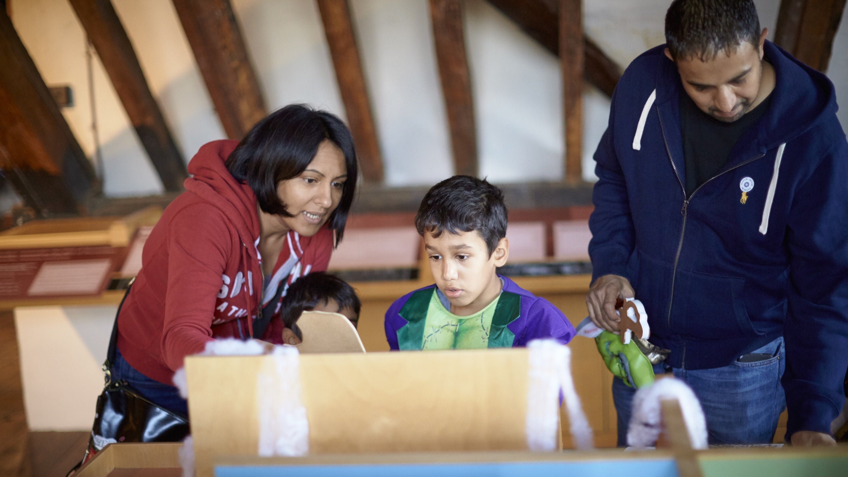 A family examine exhibits in Eastbury Manor House, Essex, with roof timbers visible above them. Eastbury is a remarkable brick-built Tudor gentry house.