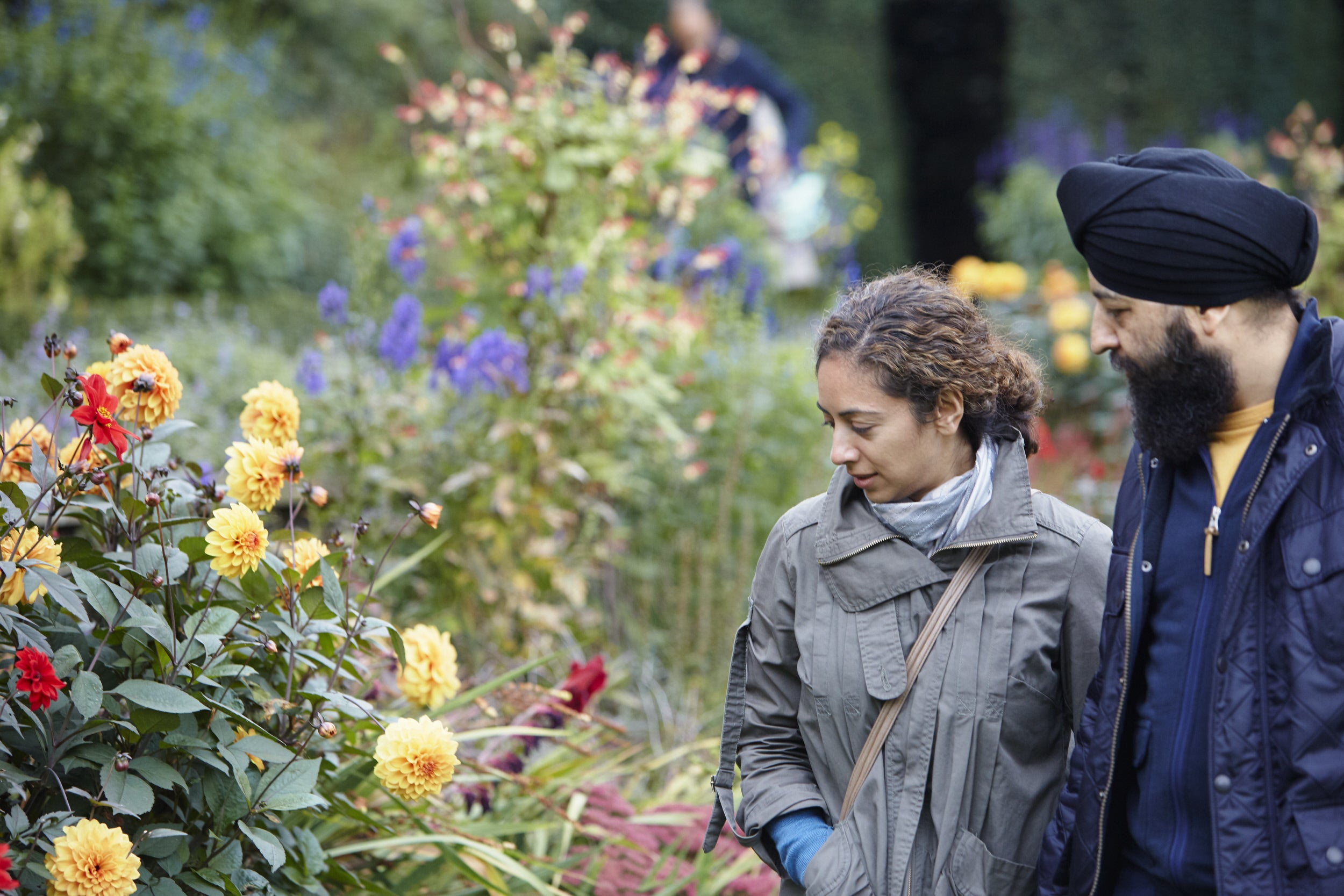 Two visitors admiring the dahlia bed which is in flower at Fenton House and Garden, with other flowering plants visible in the background.