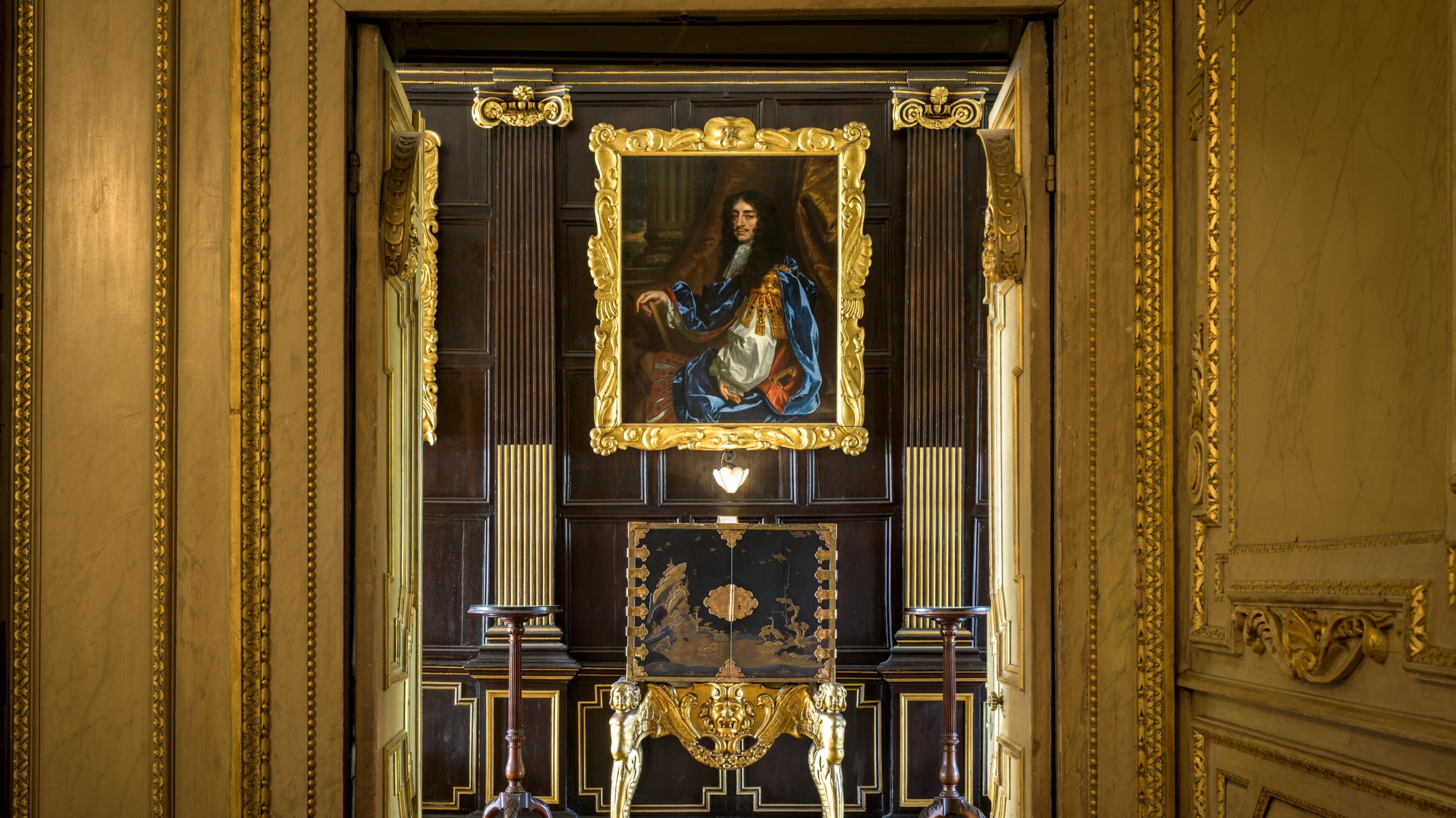 Doorframe with gold details in the foreground with a decorated cabinet beyond and a portrait above