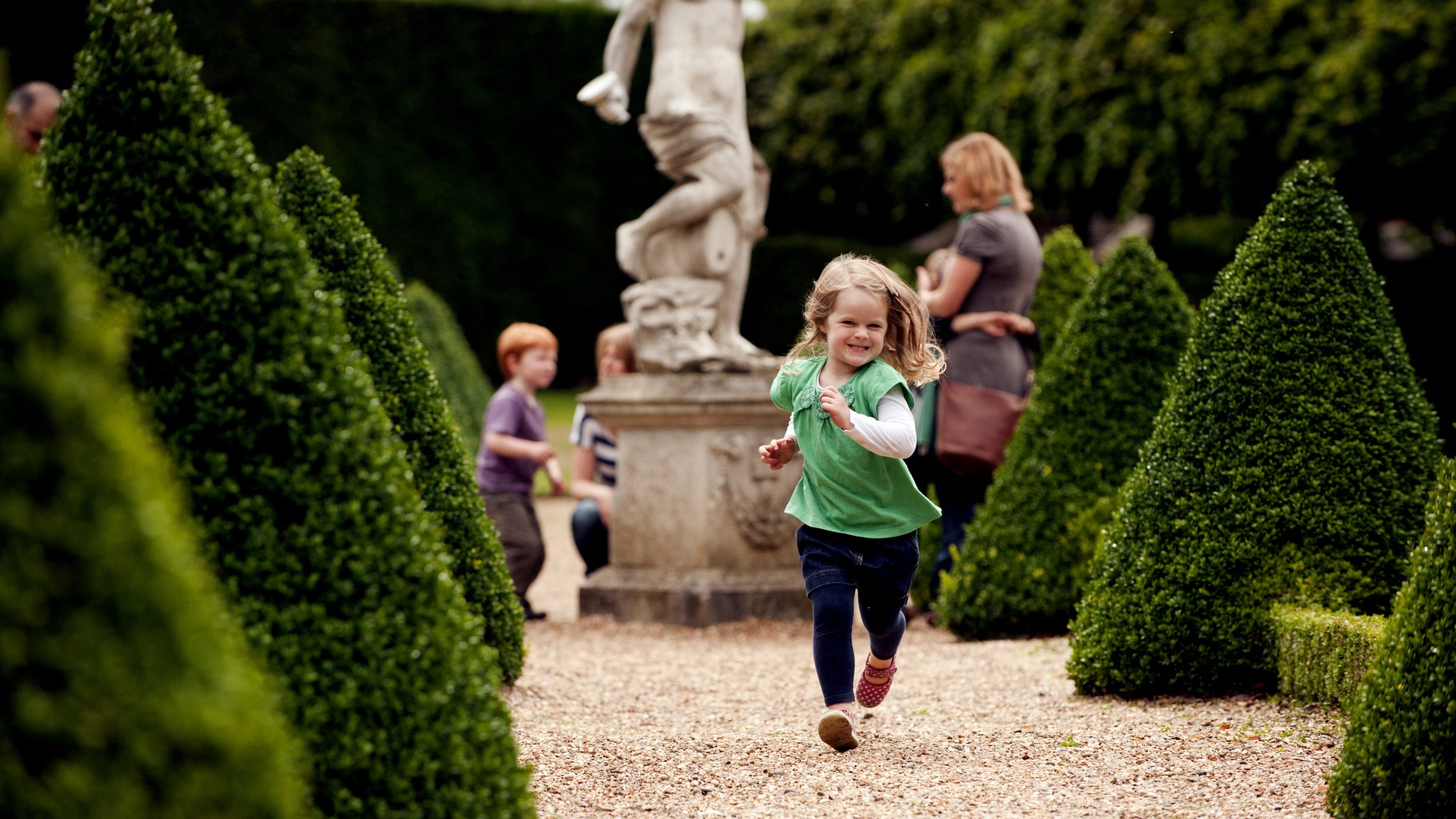 Small girl running between conical topiary hedges in the Cherry Garden at Ham House