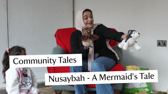 A lady sitting on a lounge chair telling a story to young children.  She is holding a plush toy in each hand to help tell the story.