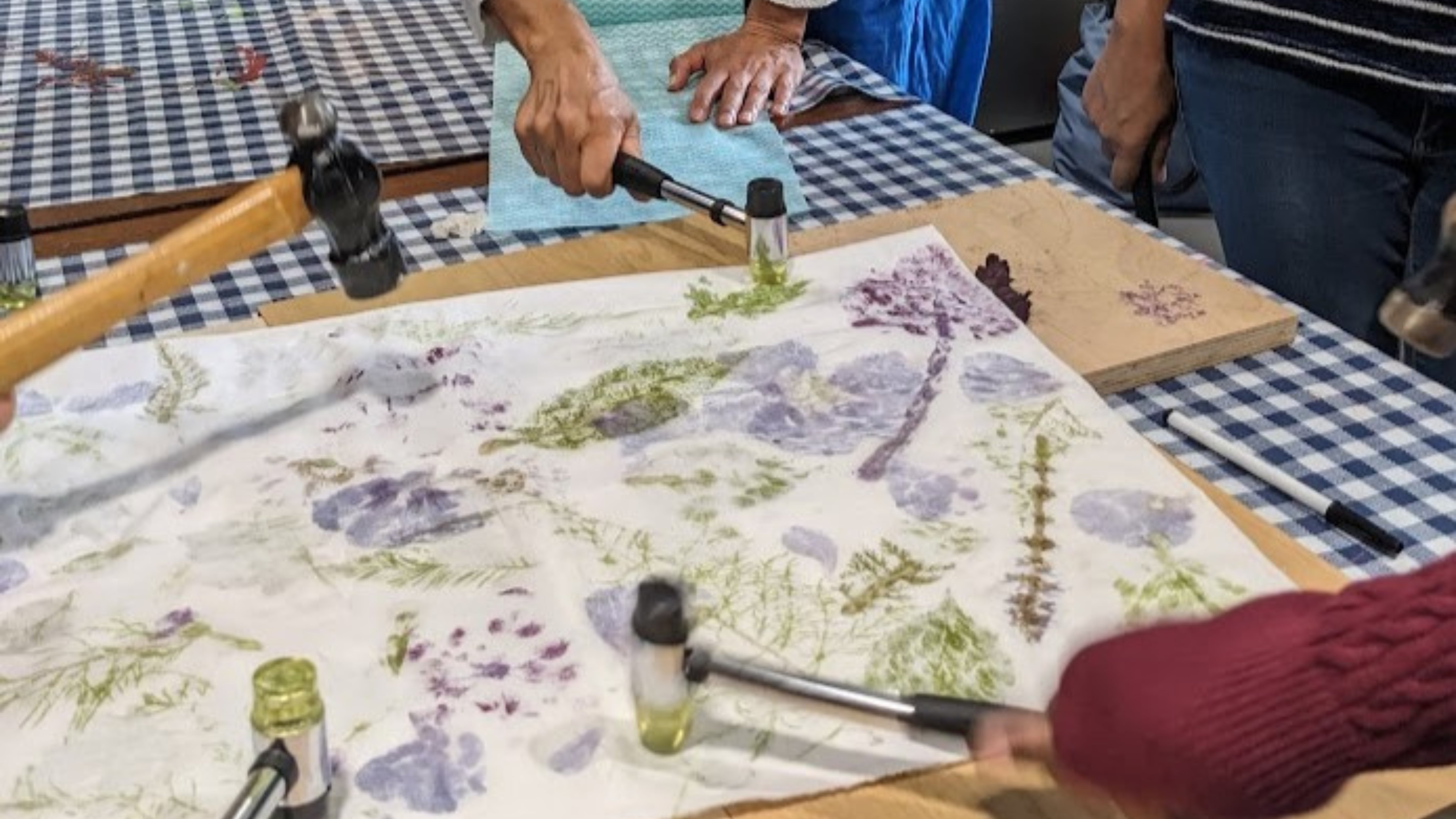 A close up of hands hammering flowers onto fabric to create an imprint.