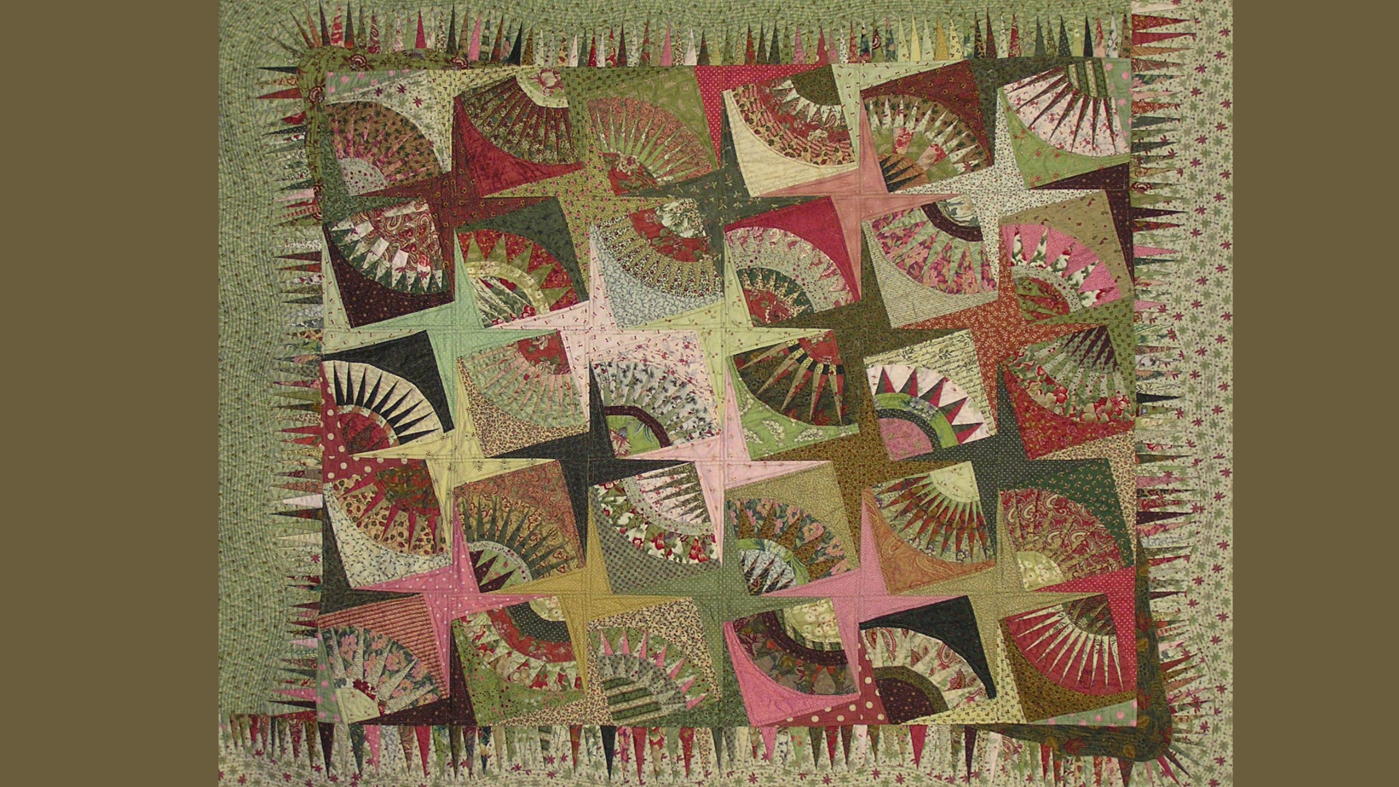 A photography of a quilt made up of square blocks, each containing a quarter-circle fan motif, the colour palette is warm earthy tones of predominantly greens with hints of pink, reds and browns.
