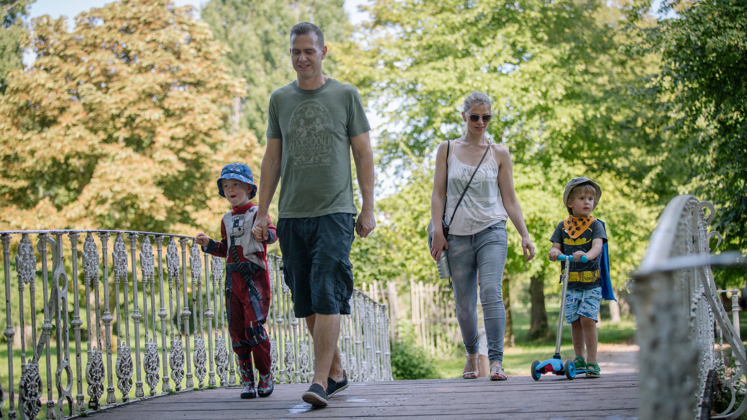 Family walking across the white bridge which spans the River Wandle at Morden Hall Park, London