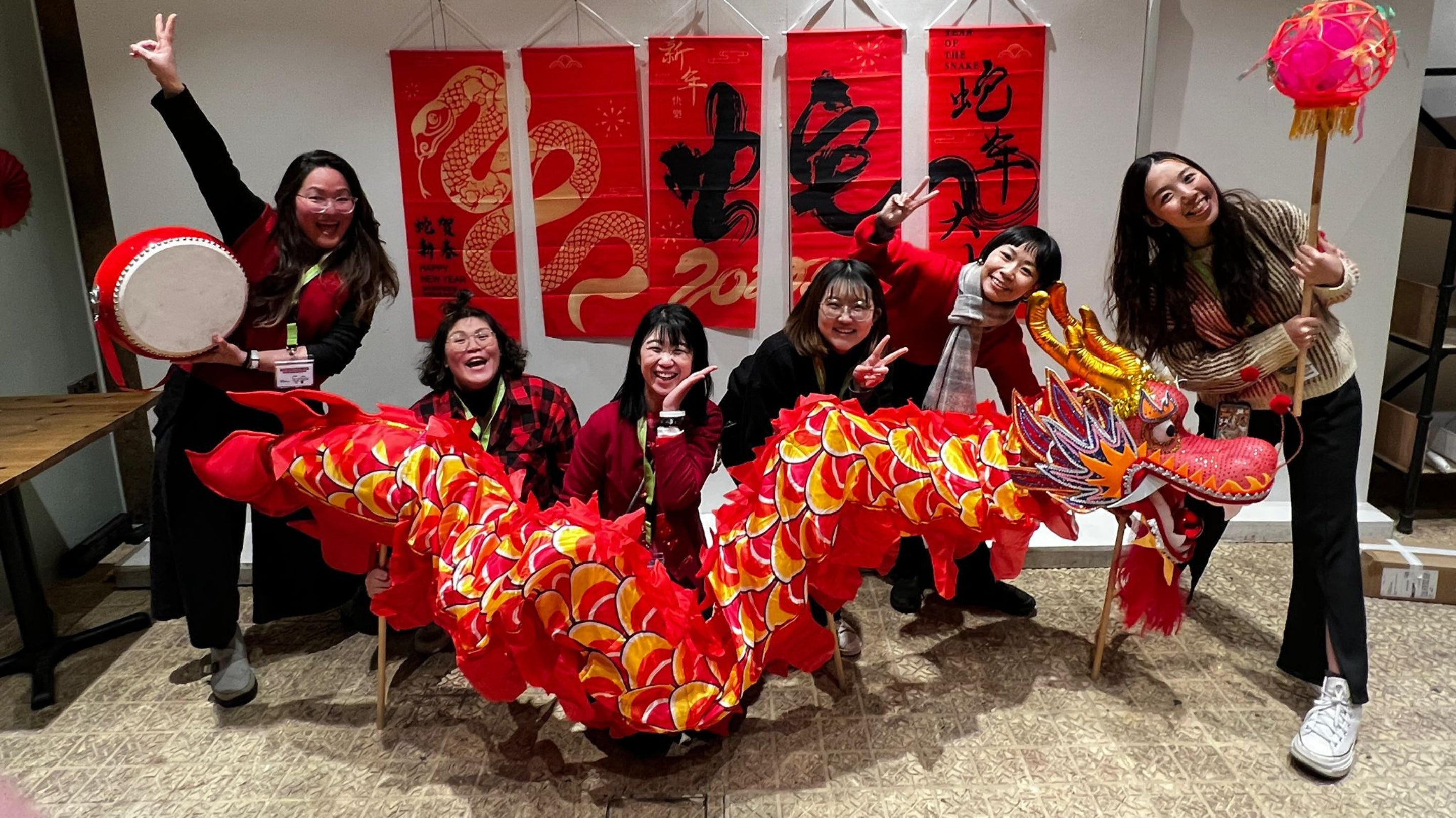 Five people, all smiling and posing, holding a large, red Chinese dragon puppet