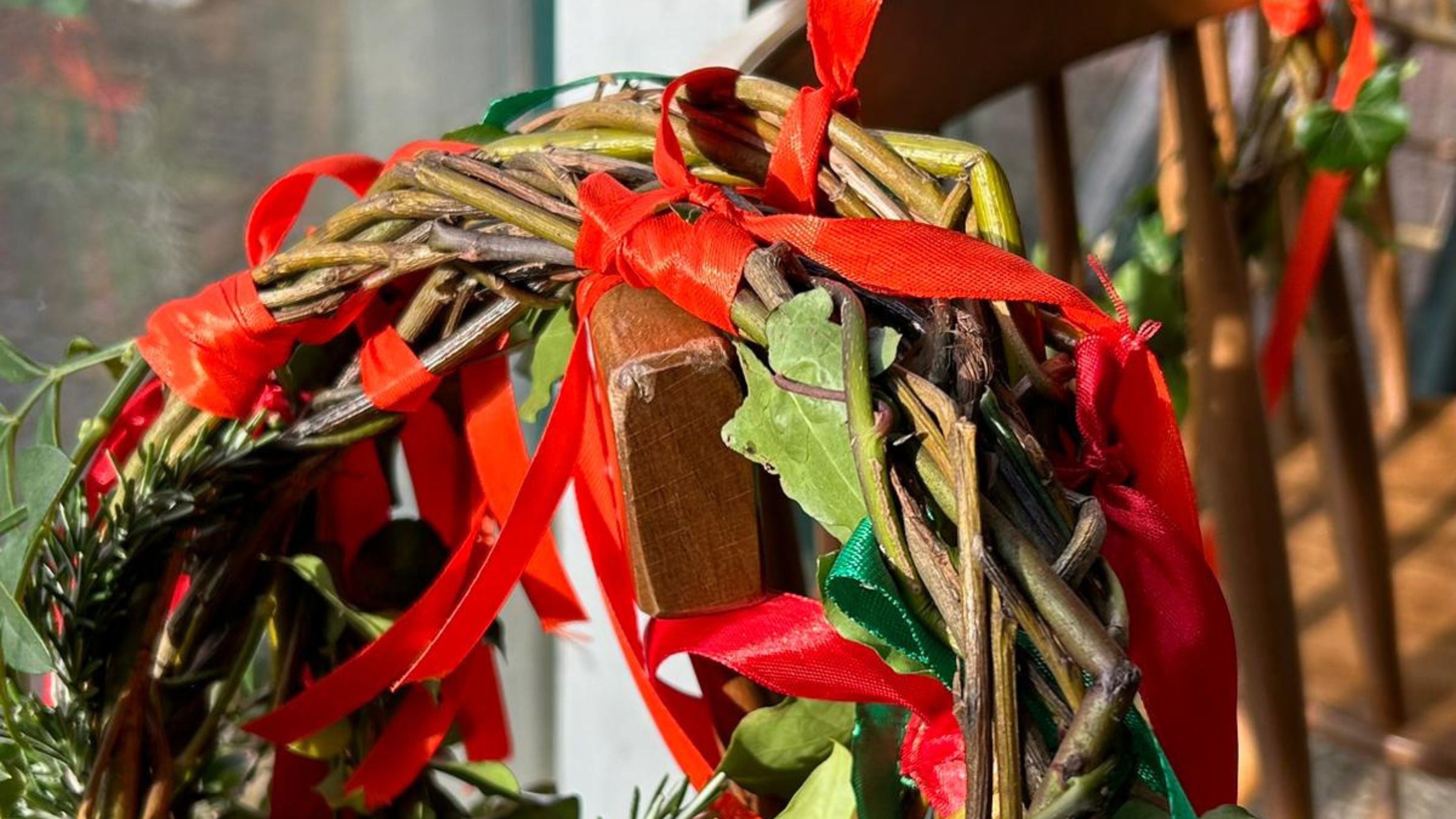 A close up of a headdress made from willow whips decorated with red ribbons and green foliage, hanging on the back of a chair