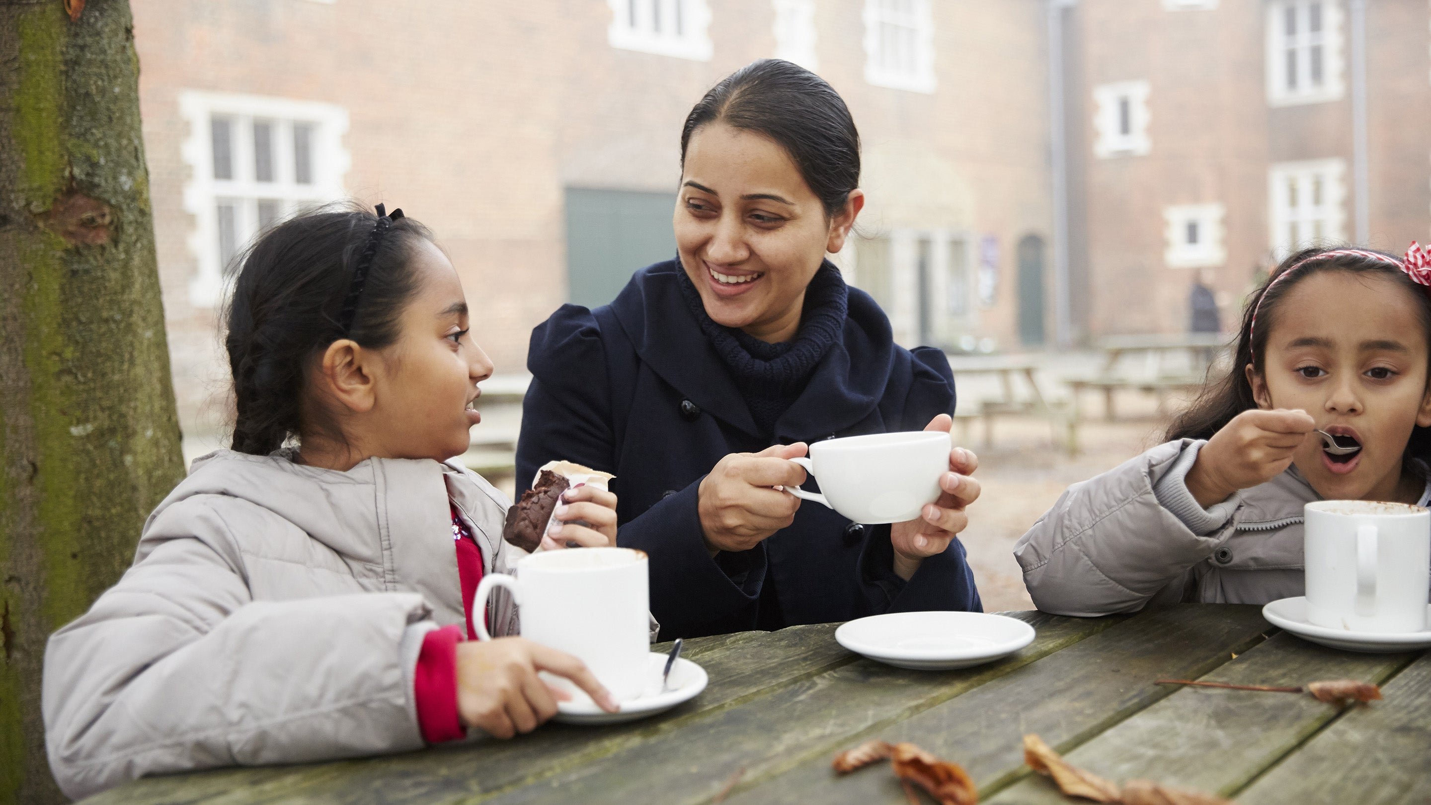 A woman and two children enjoy hot drinks sitting outside a cafe at Osterley Park and House, London