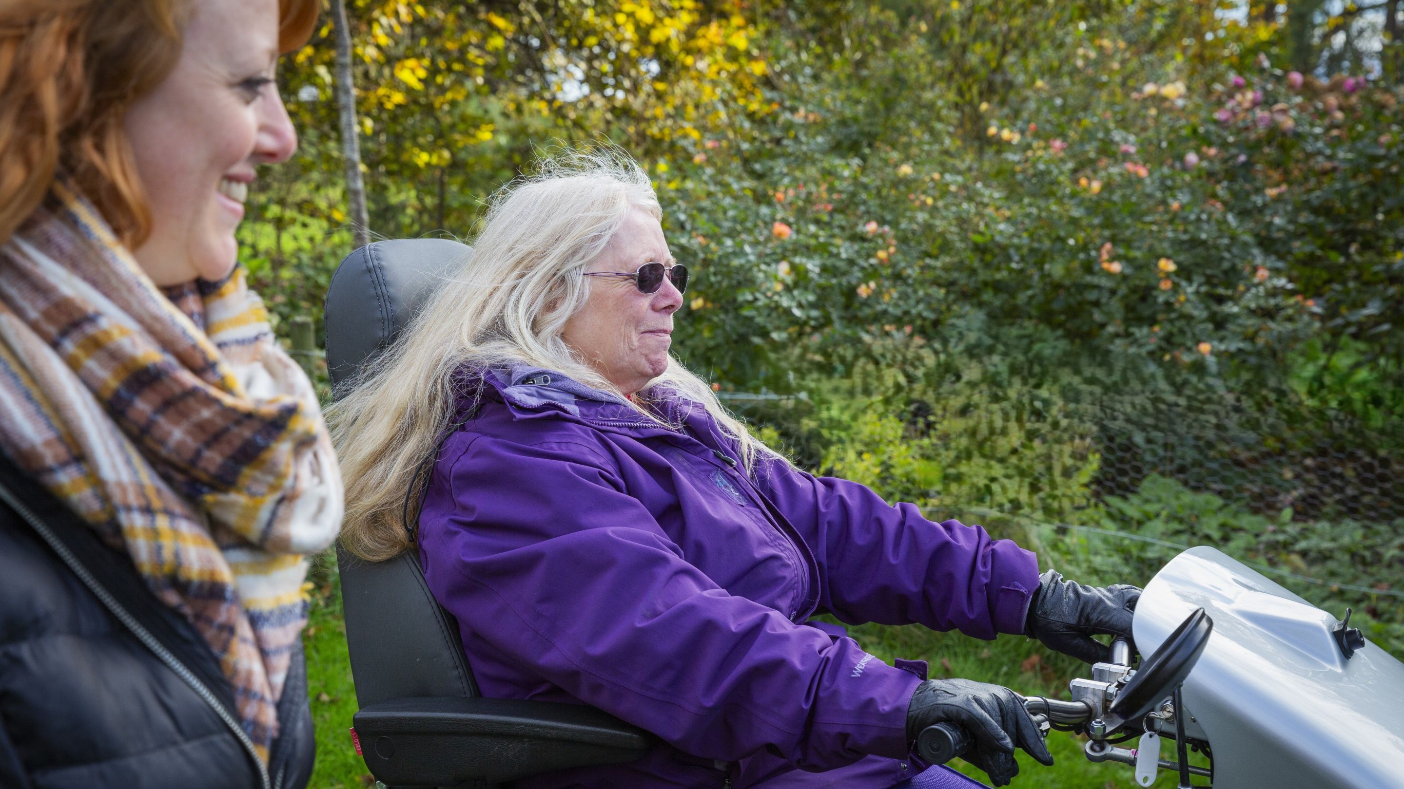 Woman on powered mobility vehicle in garden with woman walking alongside