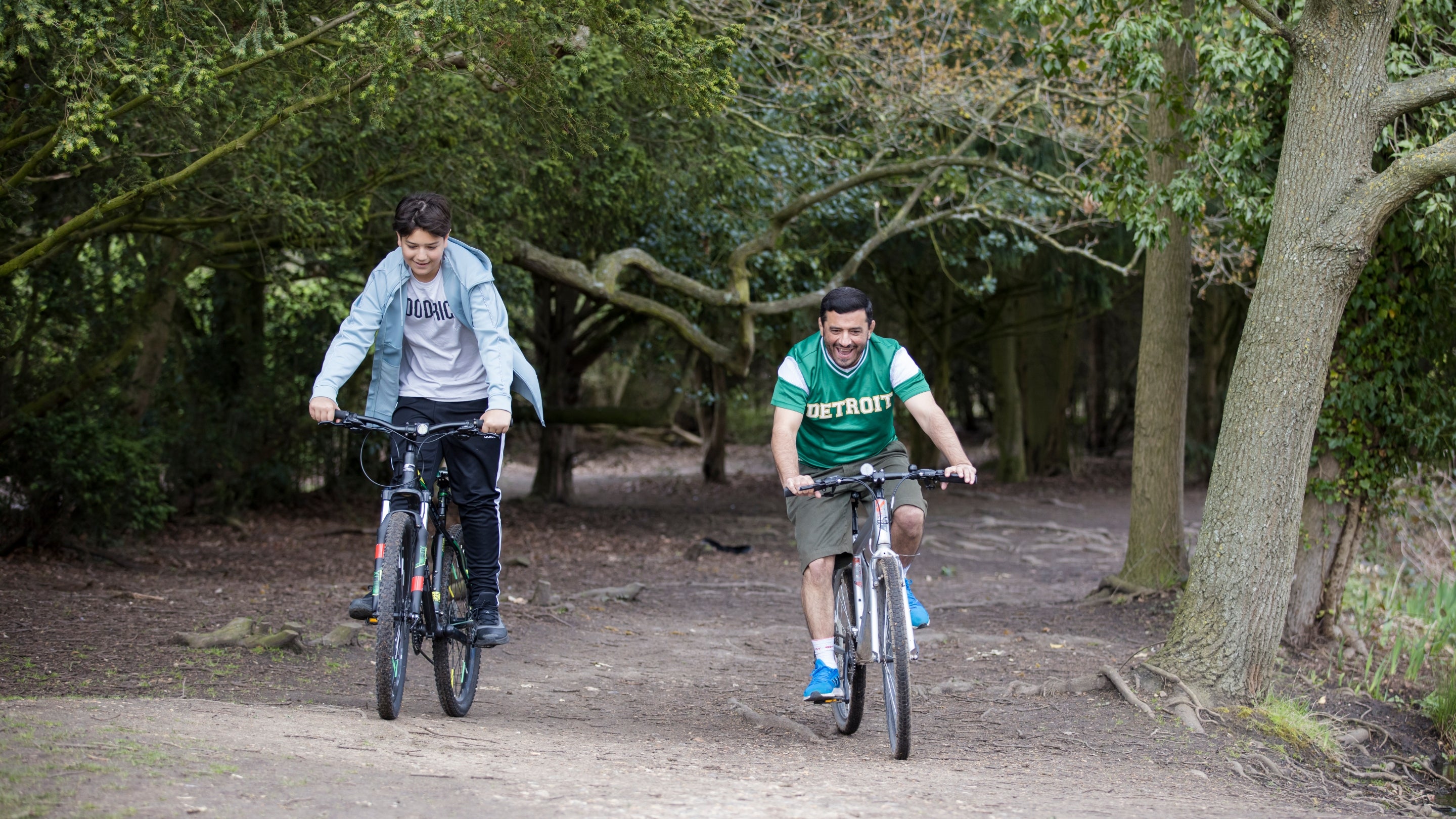 A father and teenage son cycle through woodland with wide pathways on the Osterley Park estate.