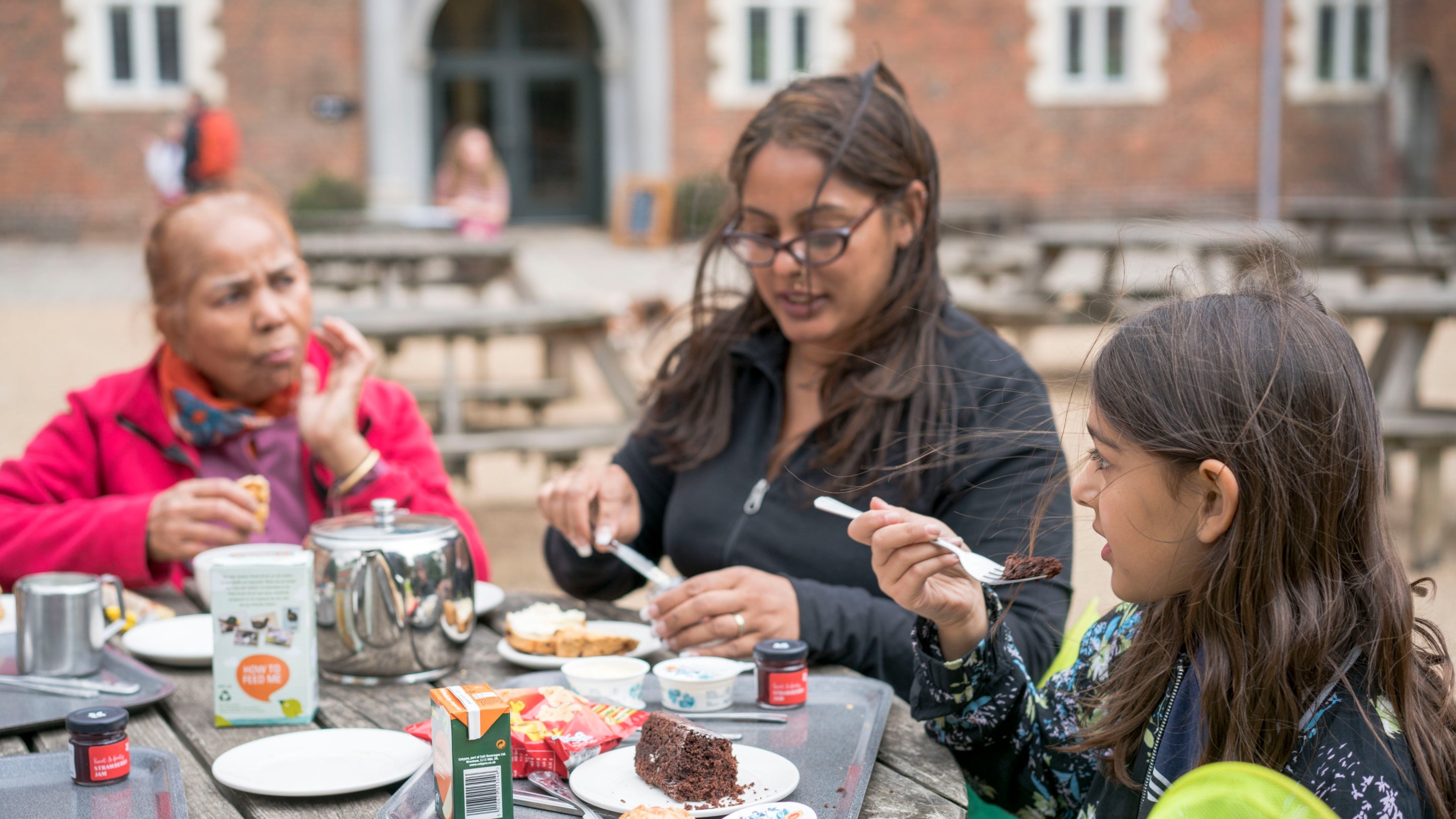 Visitors sat at a table with trays enjoying refreshments in the courtyard at Osterley Park and House, London