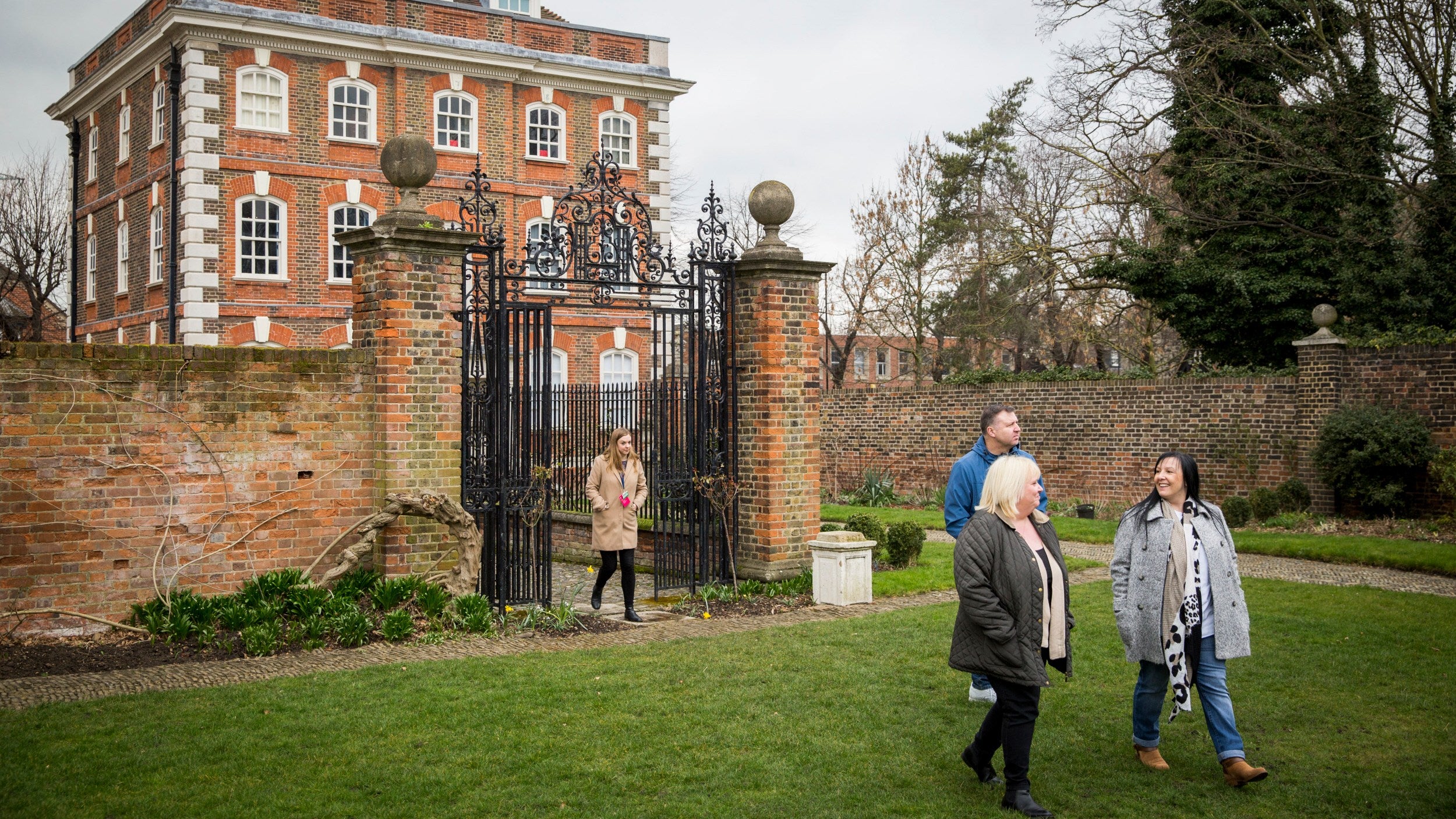 Four people leaving Rainham Hall through a set of wrought-iron gates with the house in the background