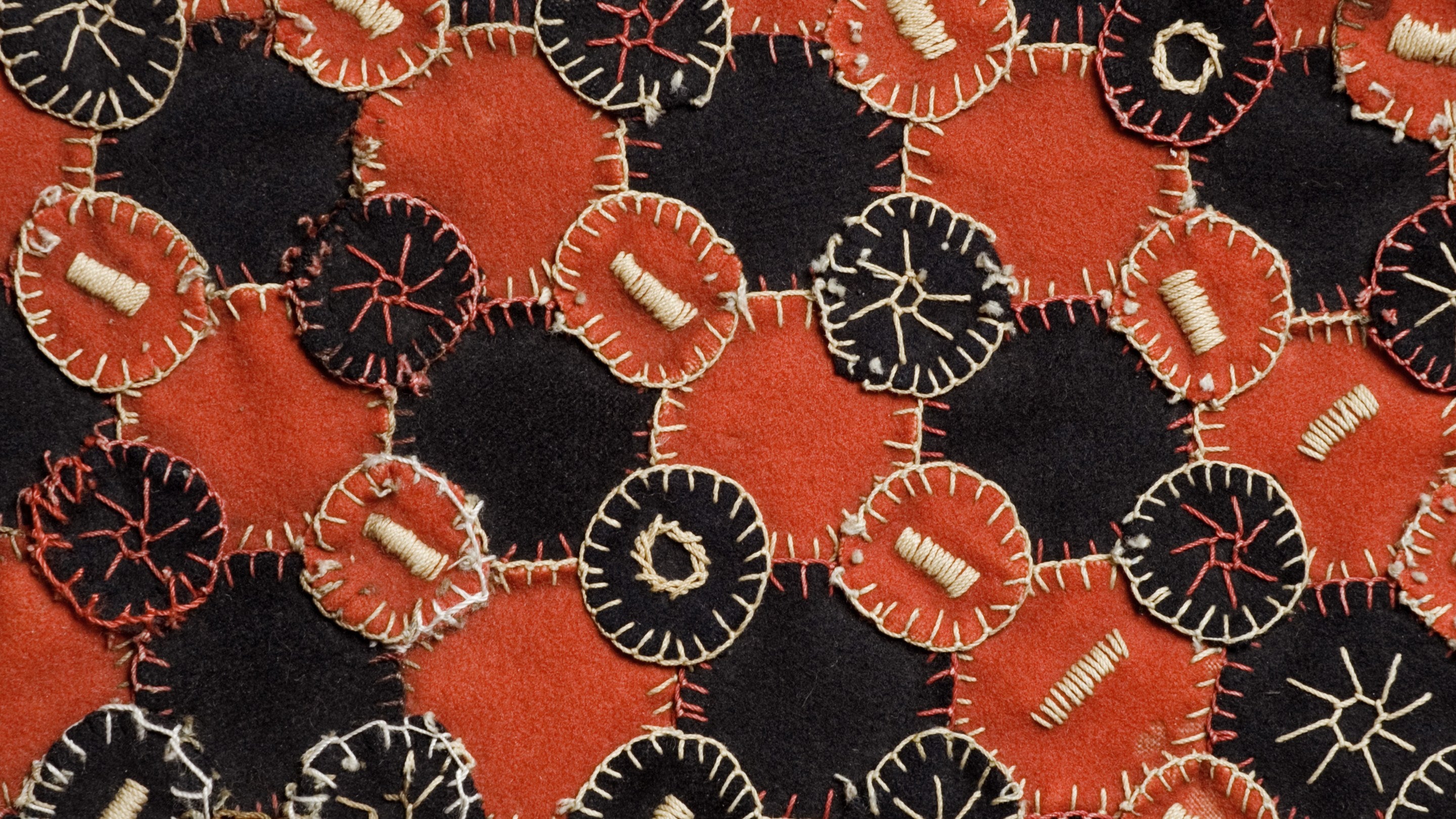 A close up detail of a hand sewn tablecloth at Carlyle's House in London with black and red squares interspersed with circles and stitched with white blanket stitch around each shape and star patterns inside each shape