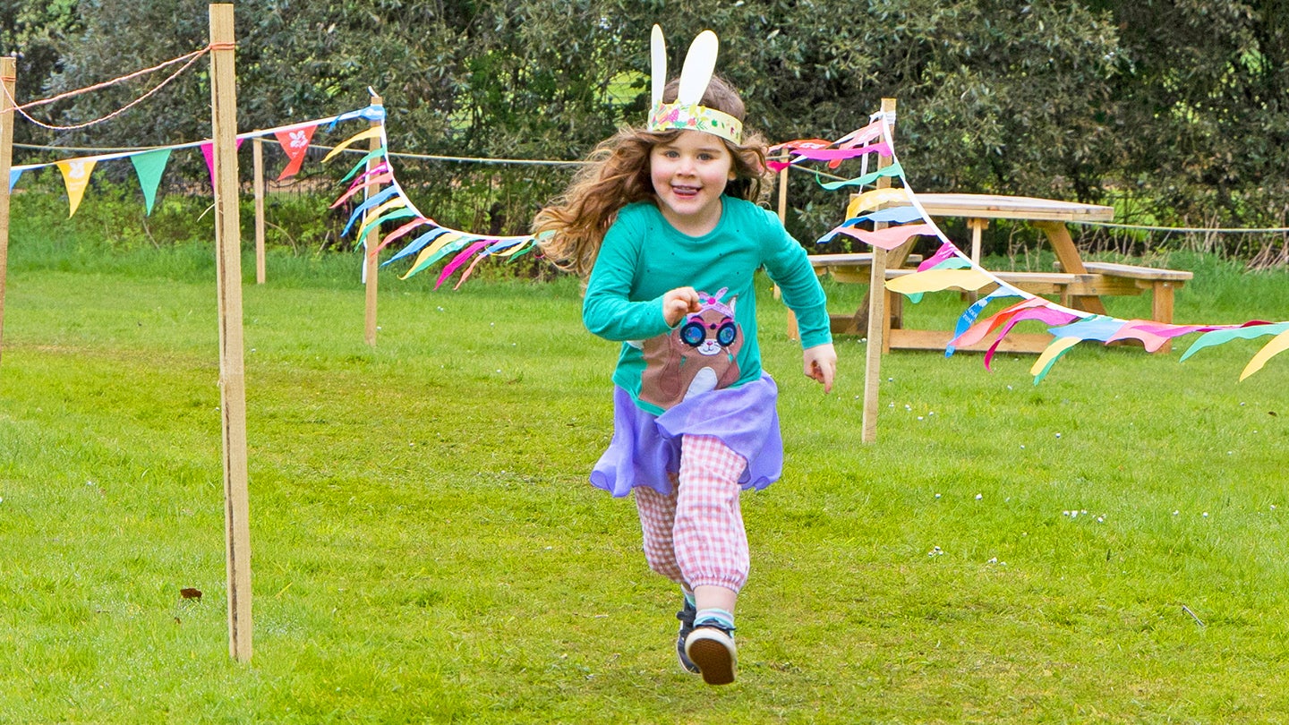 Child running around a race course marked with bunting during Easter activities at Blickling Estate, Norfolk