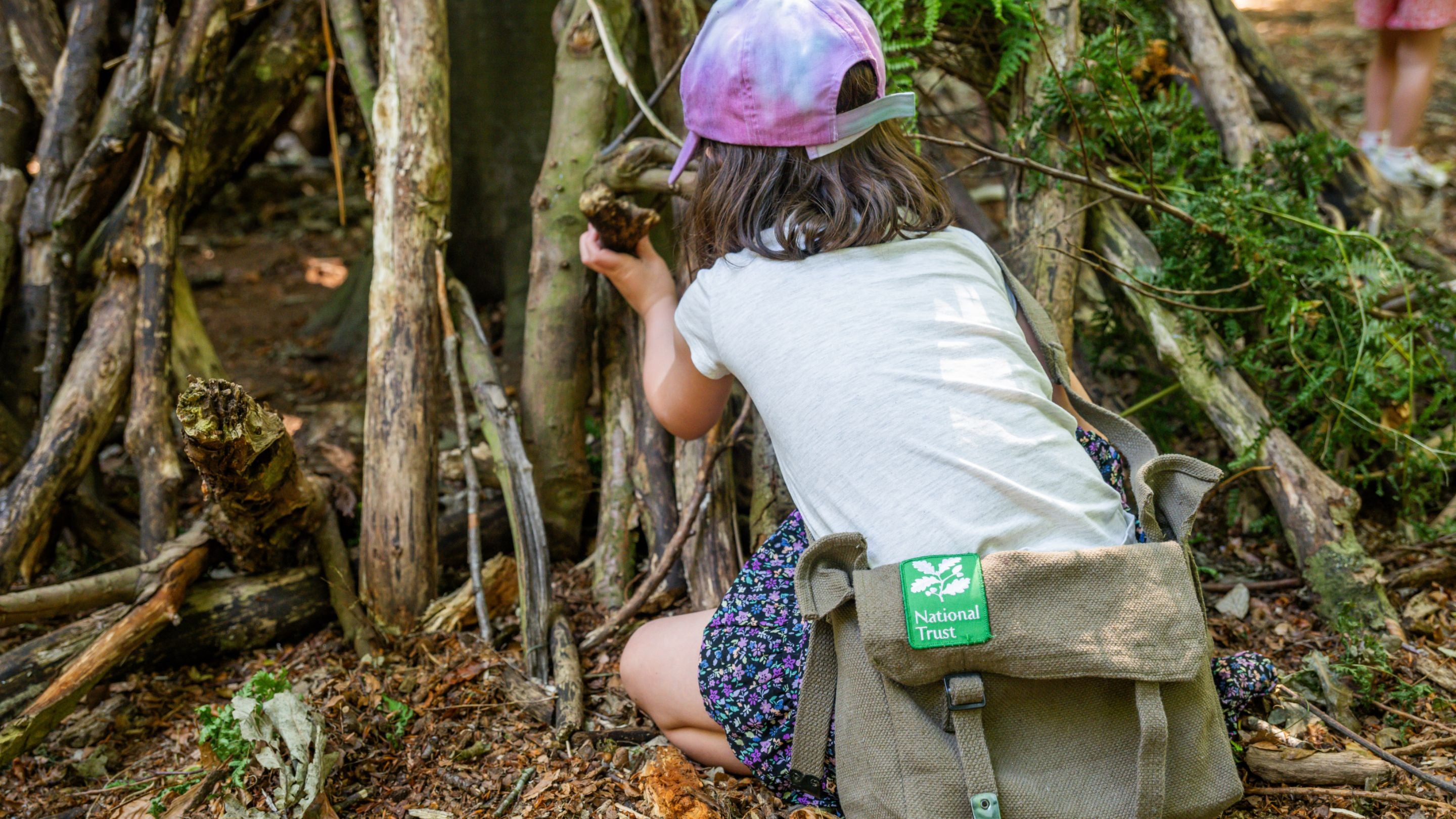 Child in the den building area at Felbrigg Estate wearing tracker pack bag, which is free to borrow.