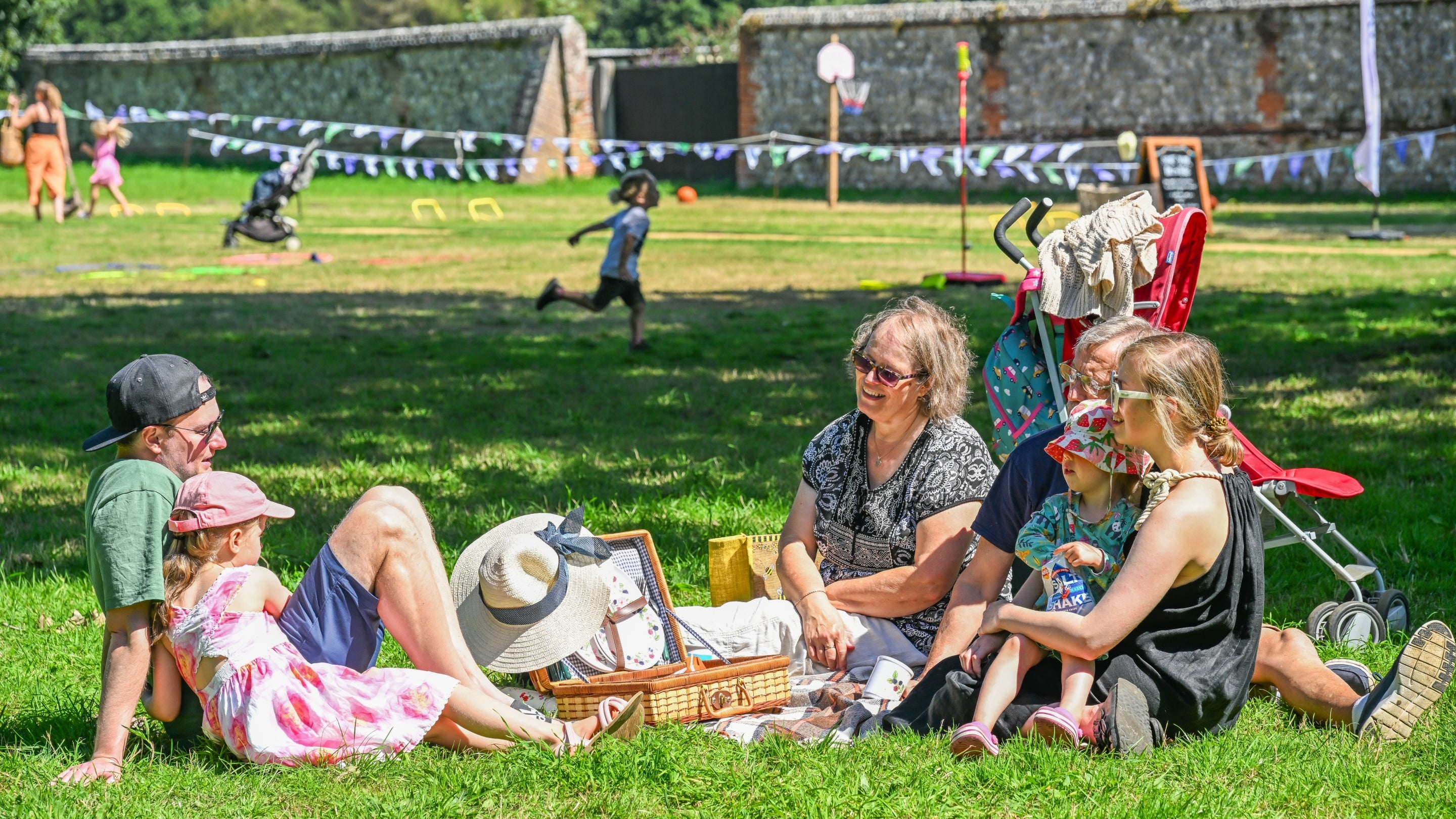 A family having a picnic on the grass as children play in the background