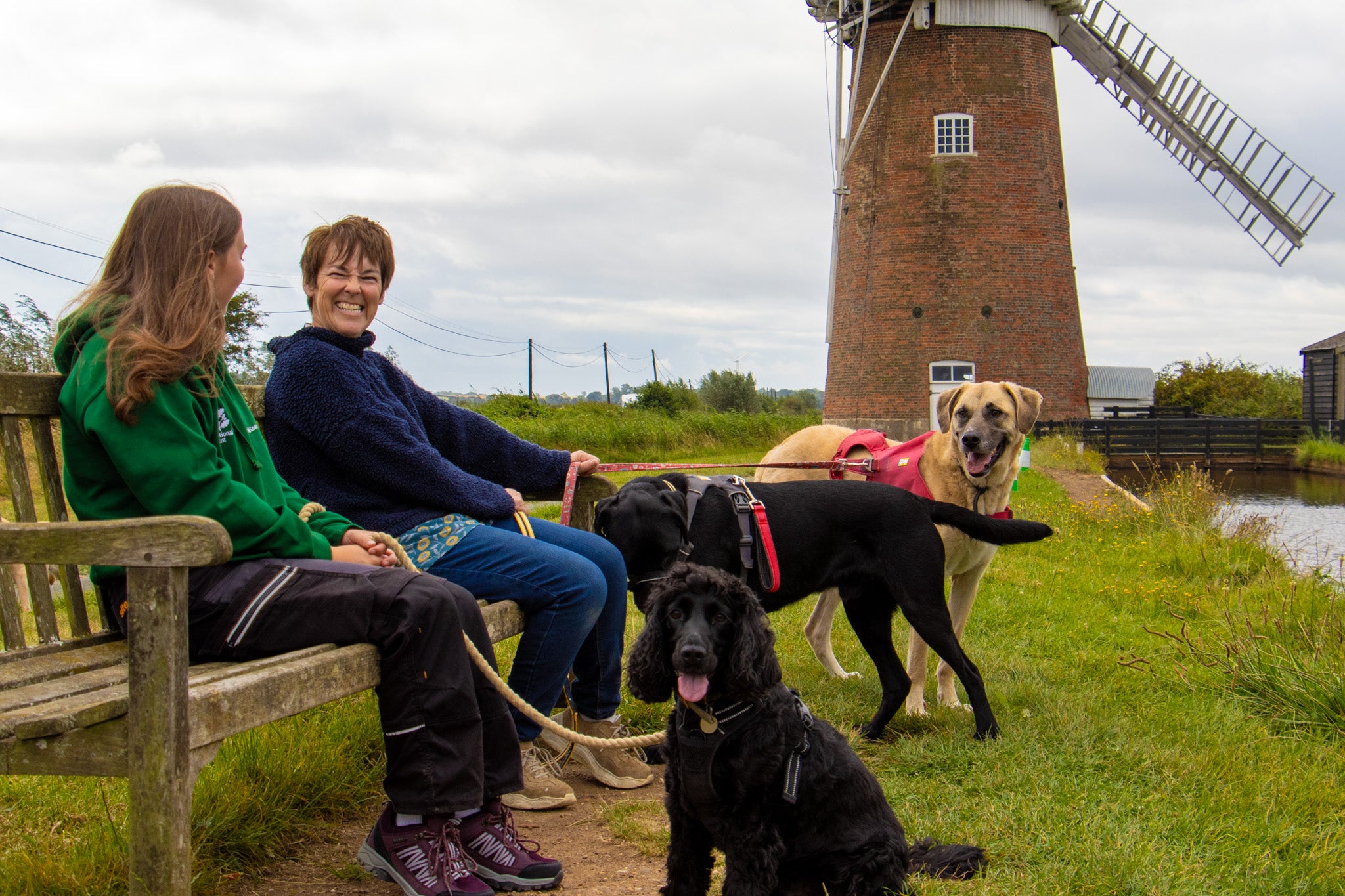 A staff member and volunteer with their dogs in front of Horsey Windpump