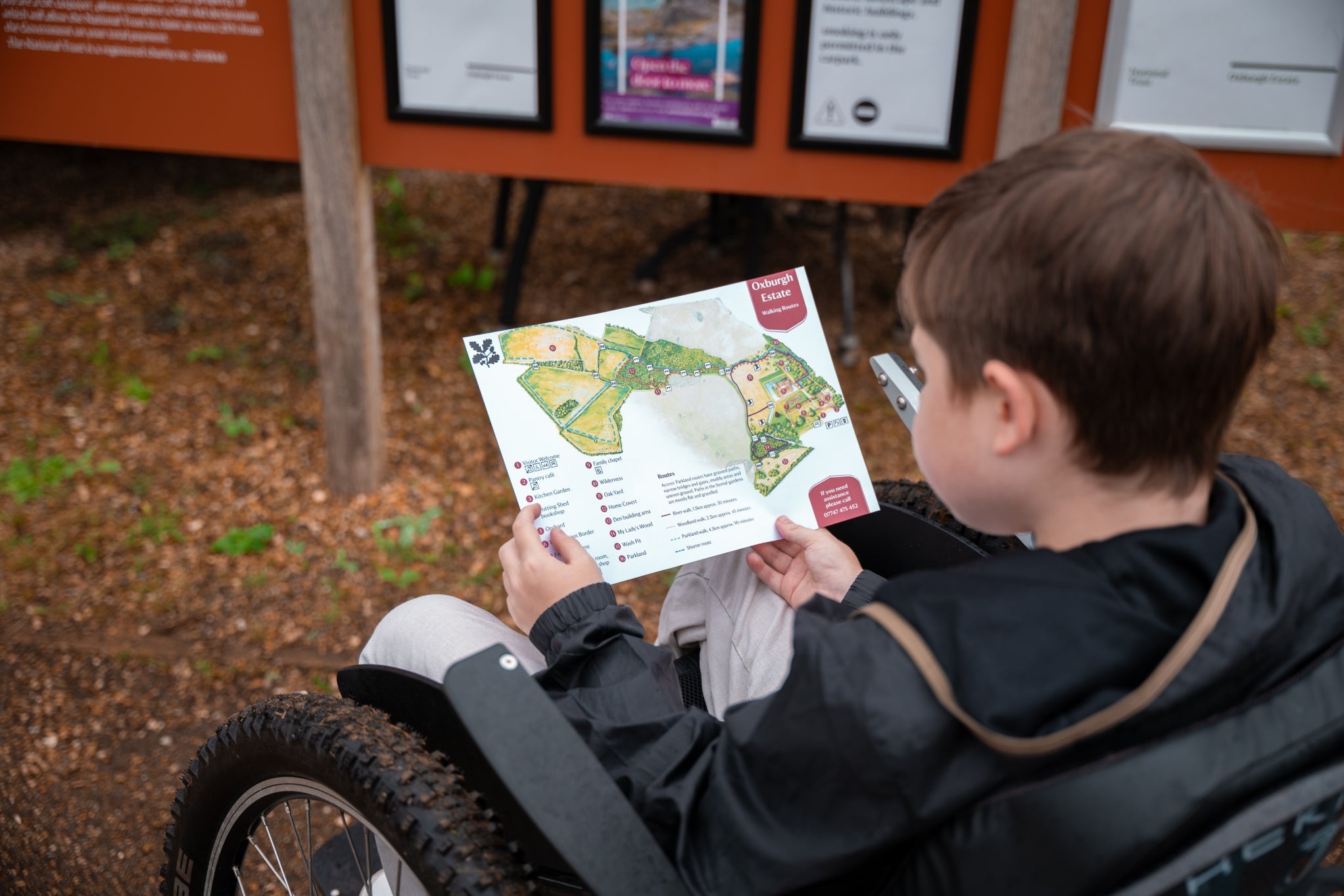 Young visitor who is a wheelchair user views a map of Oxburgh Estate