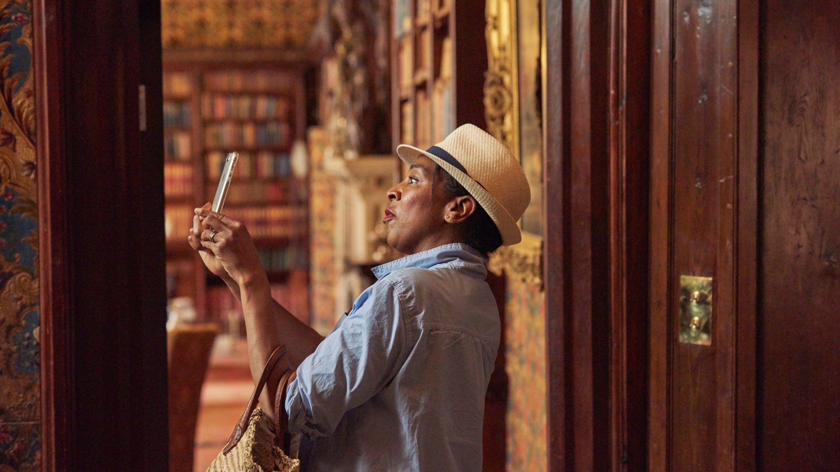 Visitor in a straw hat taking a photograph in the library at Oxburgh Estate, Norfolk