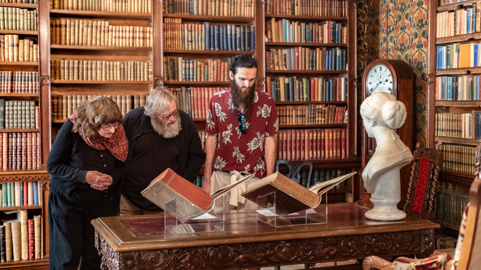 Visitors looking at books on a table in the Library at Oxburgh Hall, Norfolk with bookcases in the background